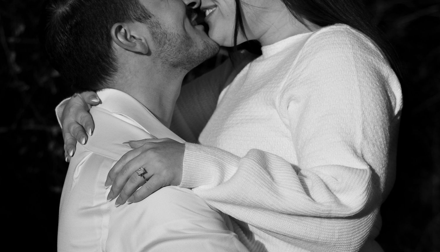 Romantic black and white photo of couple sharing a kiss in close intimate embrace outdoors.