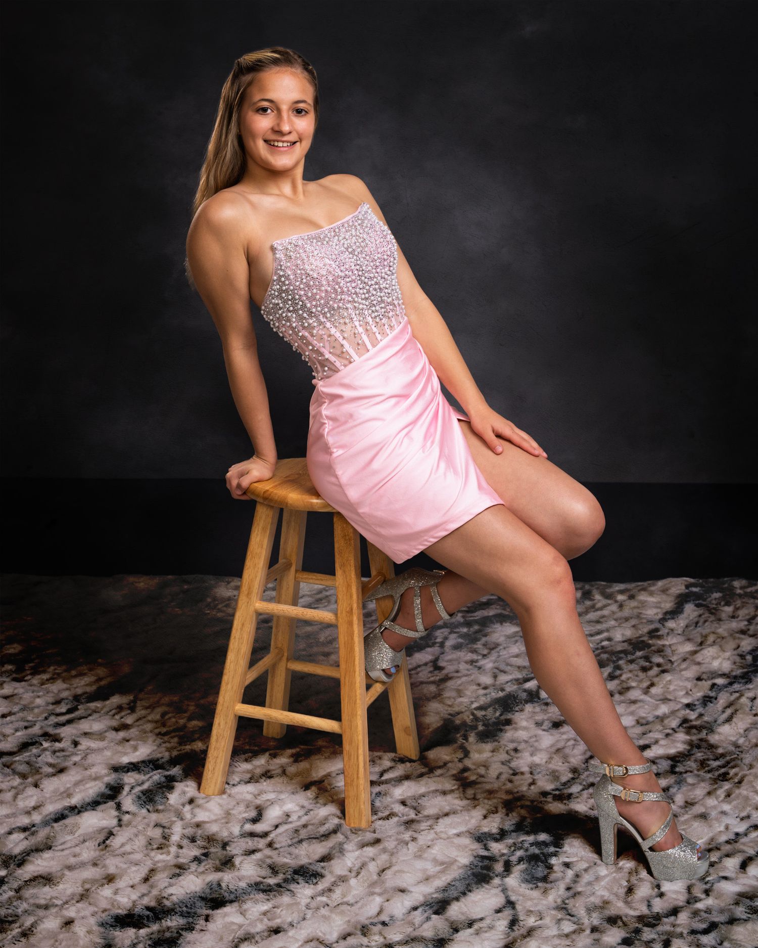 Teen girl in pink strapless embellished dress poses on wooden stool.