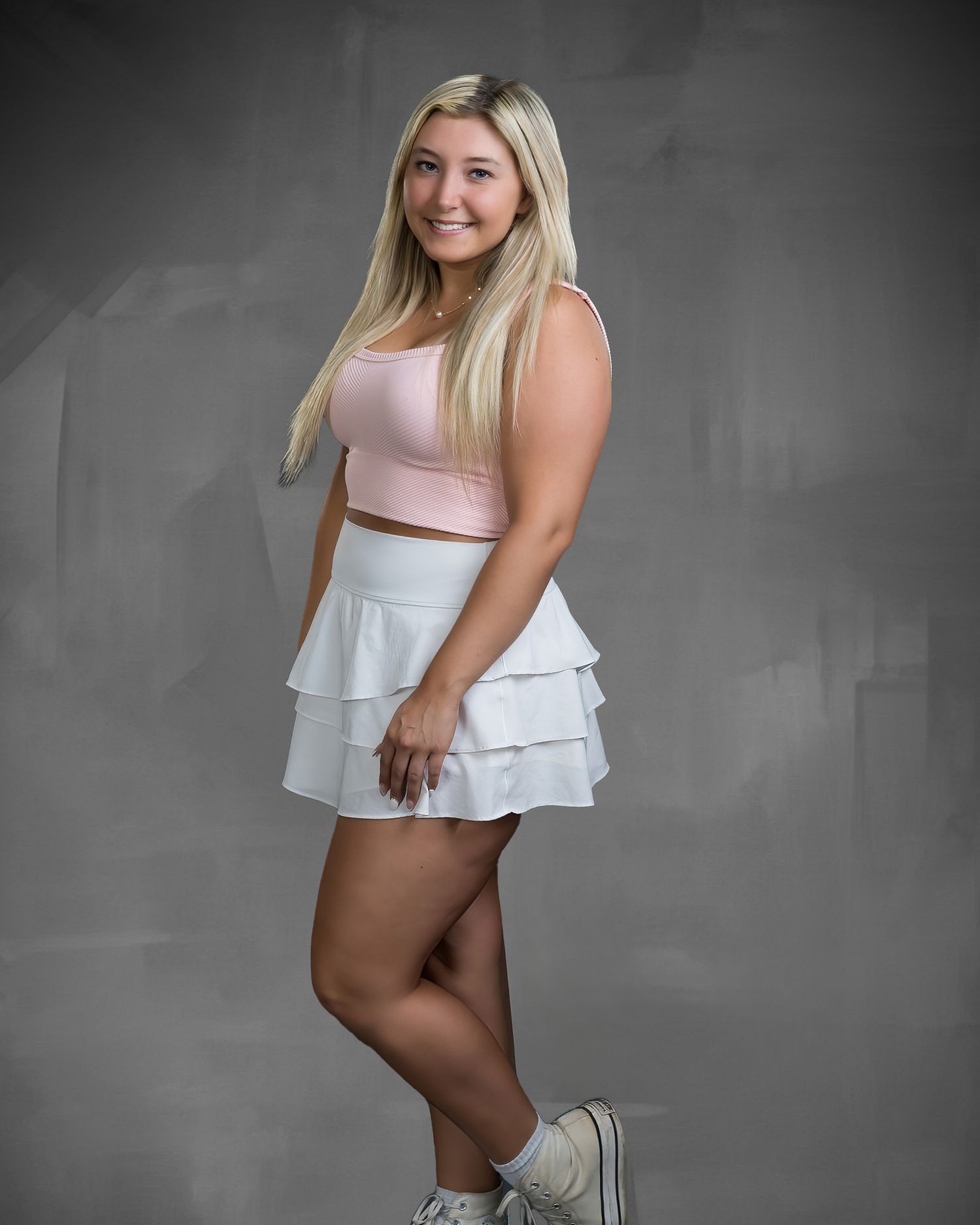 Blonde teenage girl in pink crop top and white ruffle skirt poses for senior portrait.