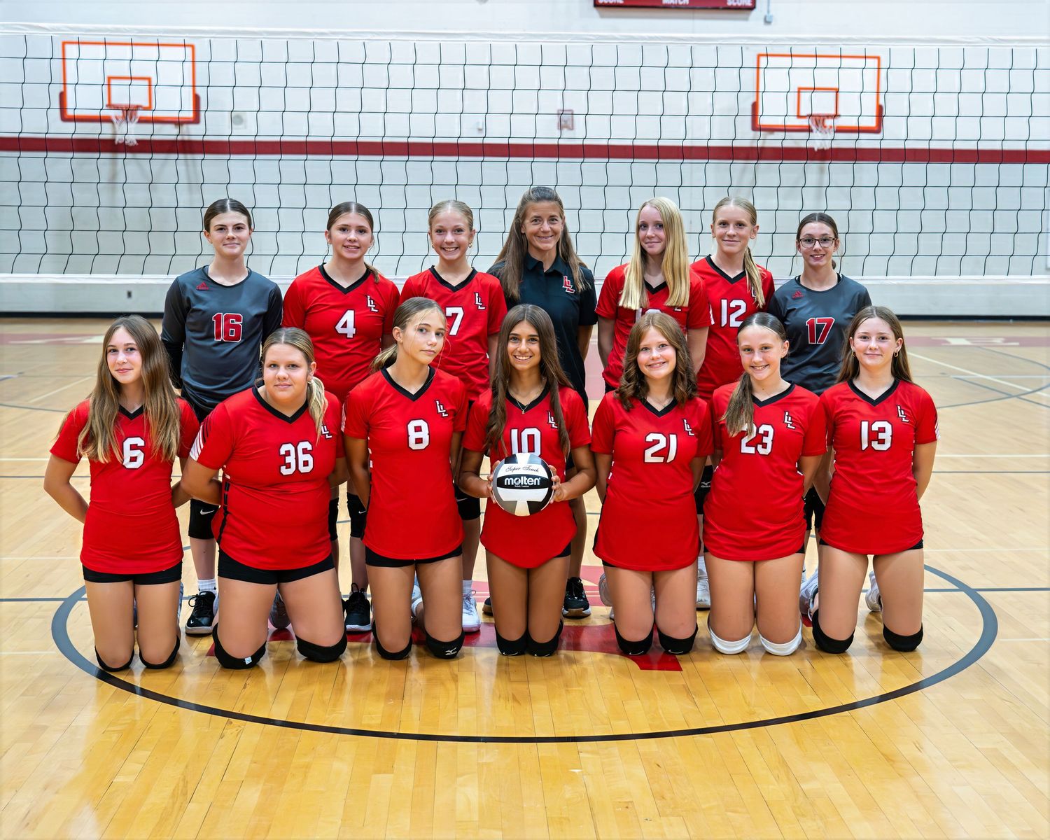 Girls volleyball team in red and black uniforms posing for team photo on court.