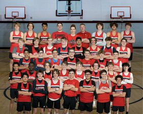 Large boys basketball team poses in red uniforms inside gymnasium for official team photo.
