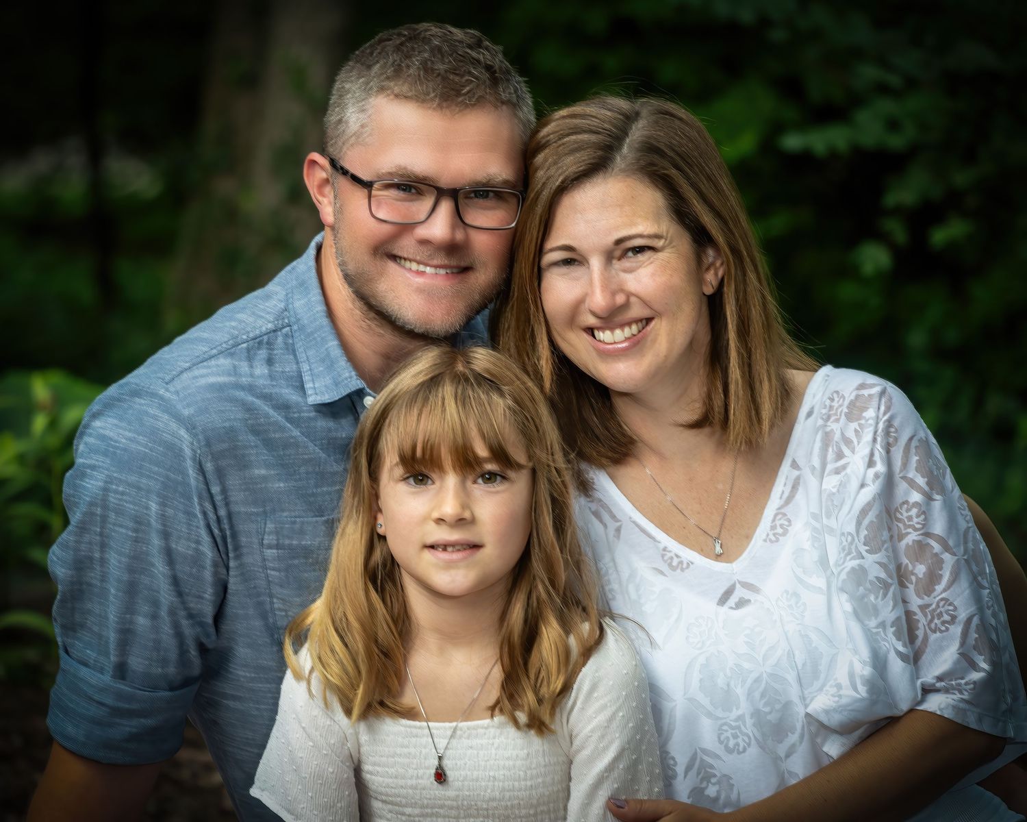 Family of three with parents and young daughter posing outdoors in garden.
