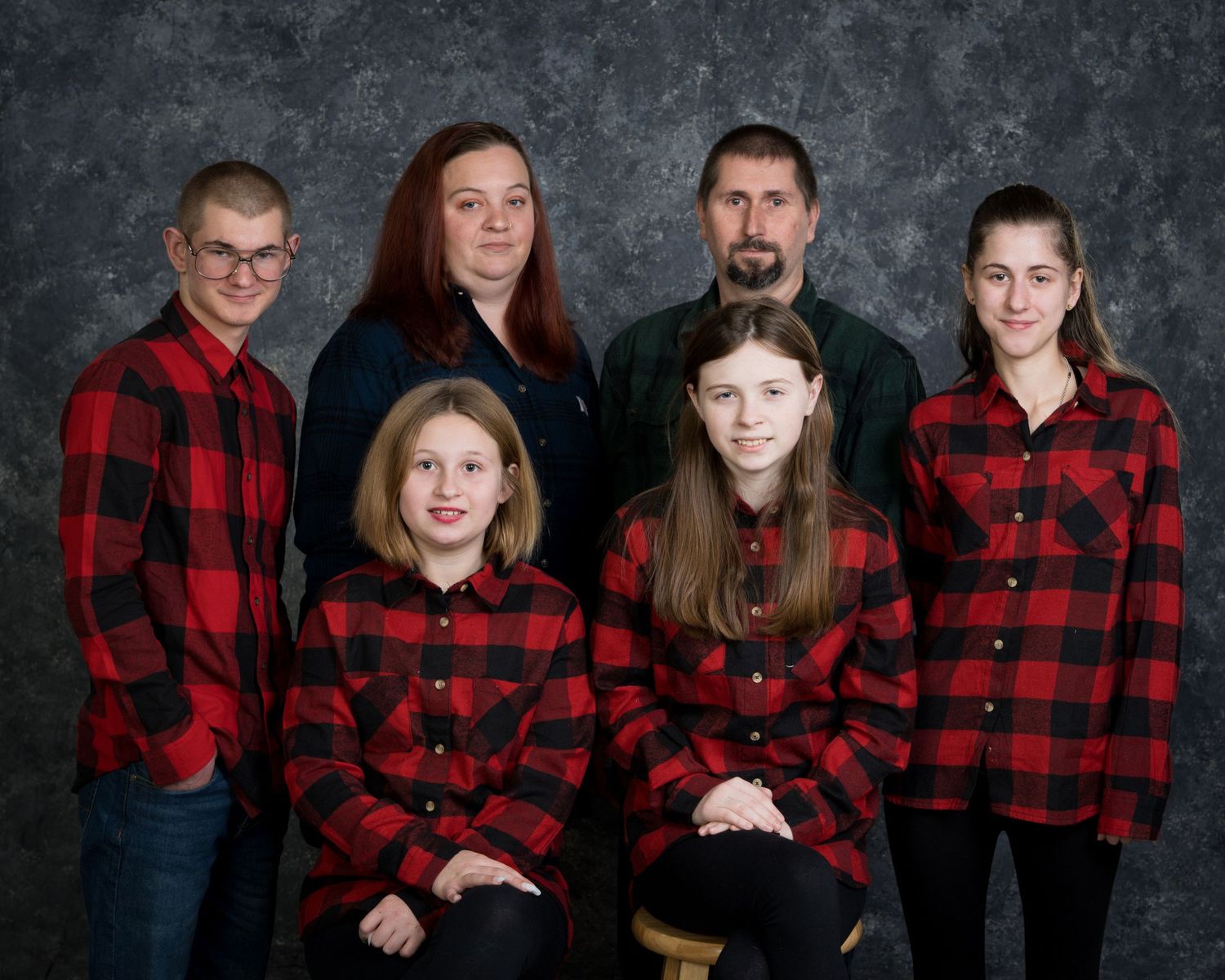 Family of six wearing matching red buffalo plaid flannel shirts posing for a studio portrait photo.