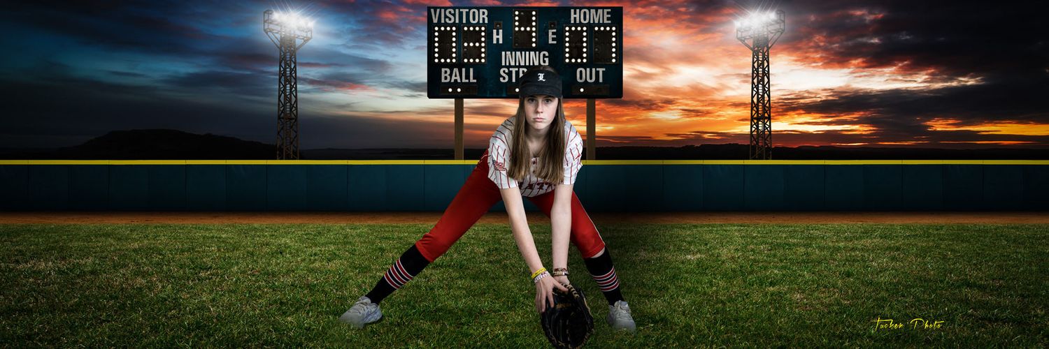 Female softball player posing dramatically on a field at sunset with a scoreboard in the background.