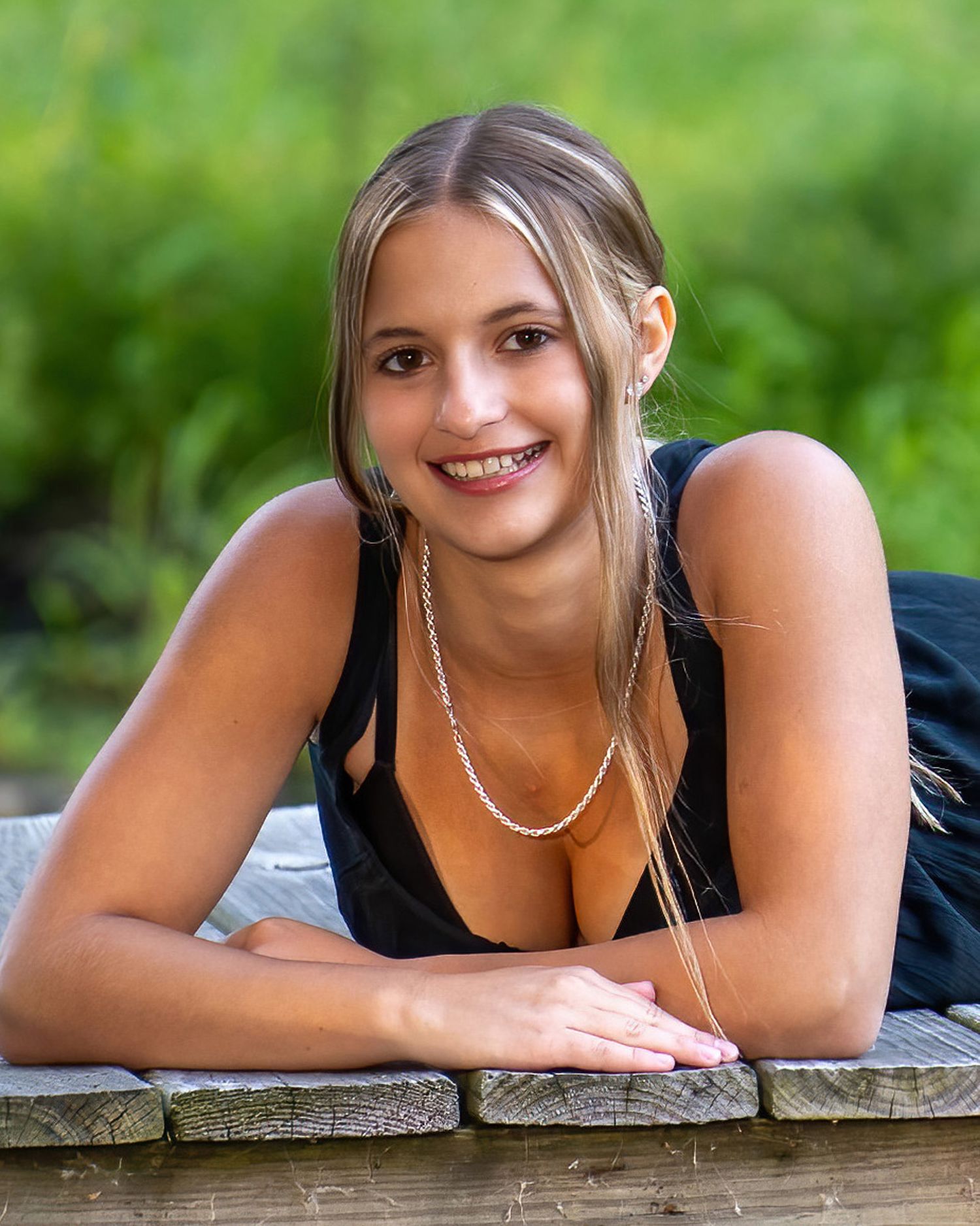 Smiling young blonde woman leaning on a wooden railing outdoors in a black top.