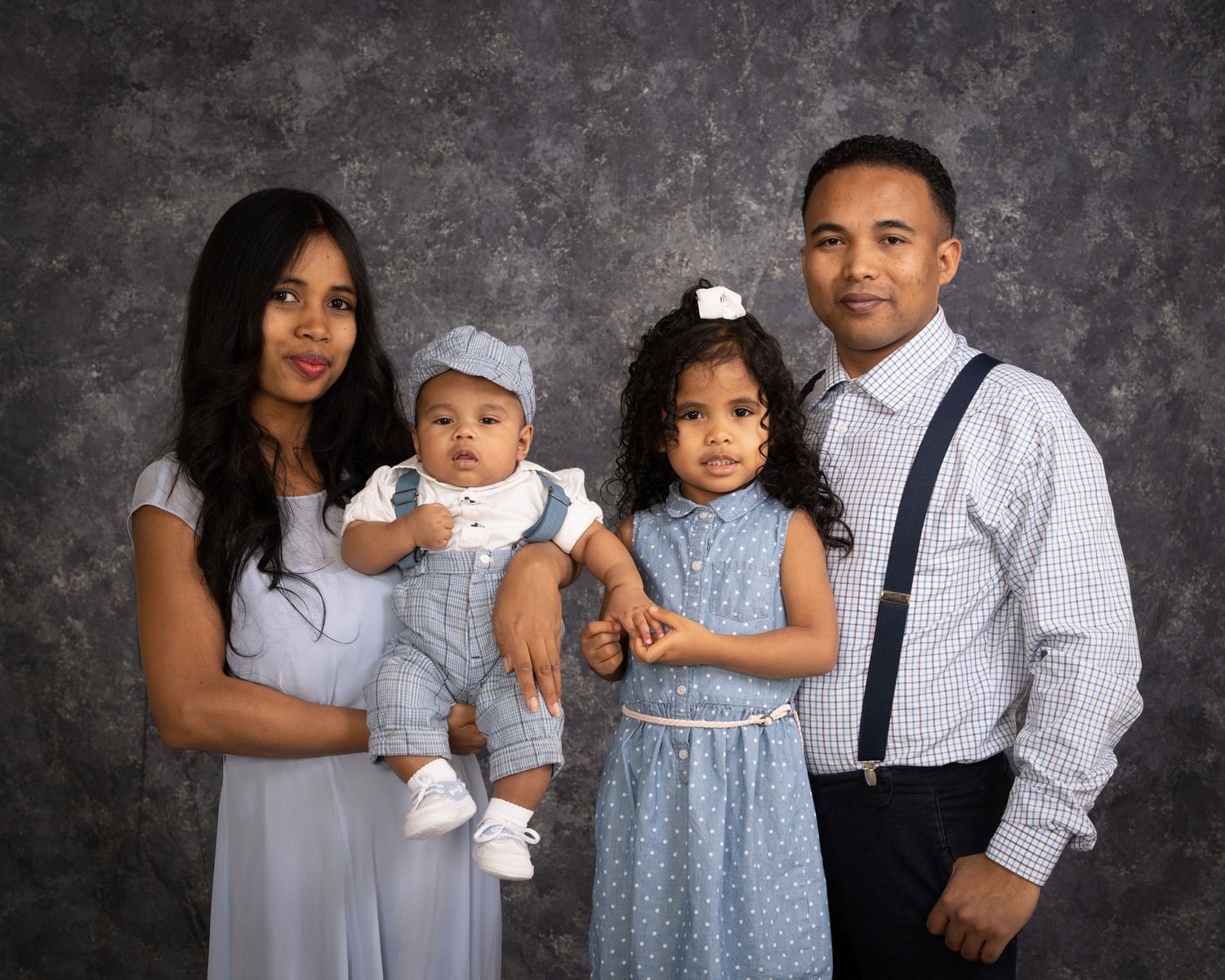 Family portrait with parents and two young children in coordinating blue outfits.
