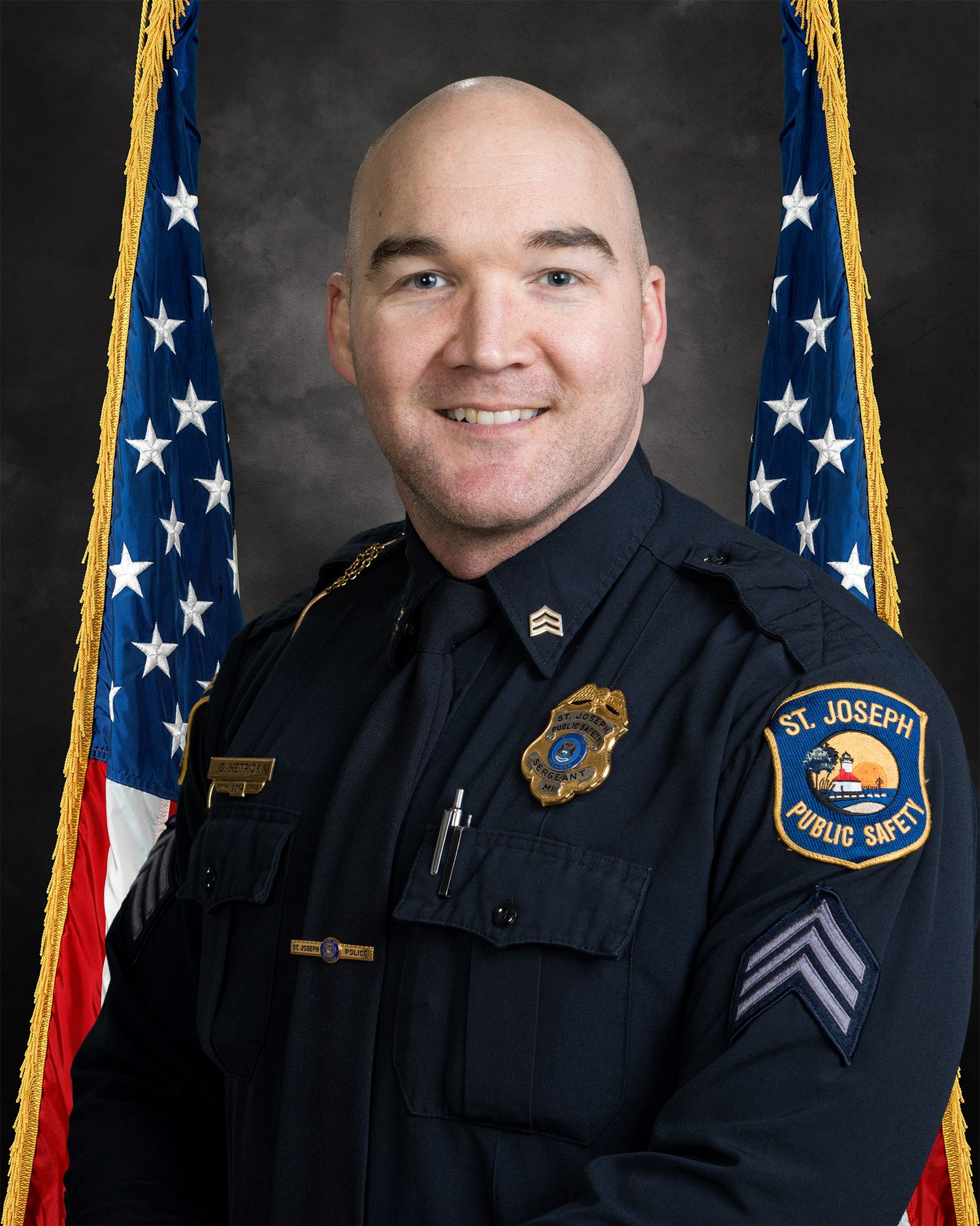 St. Joseph Public Safety sergeant in uniform with badge smiling in an official portrait before American flags.