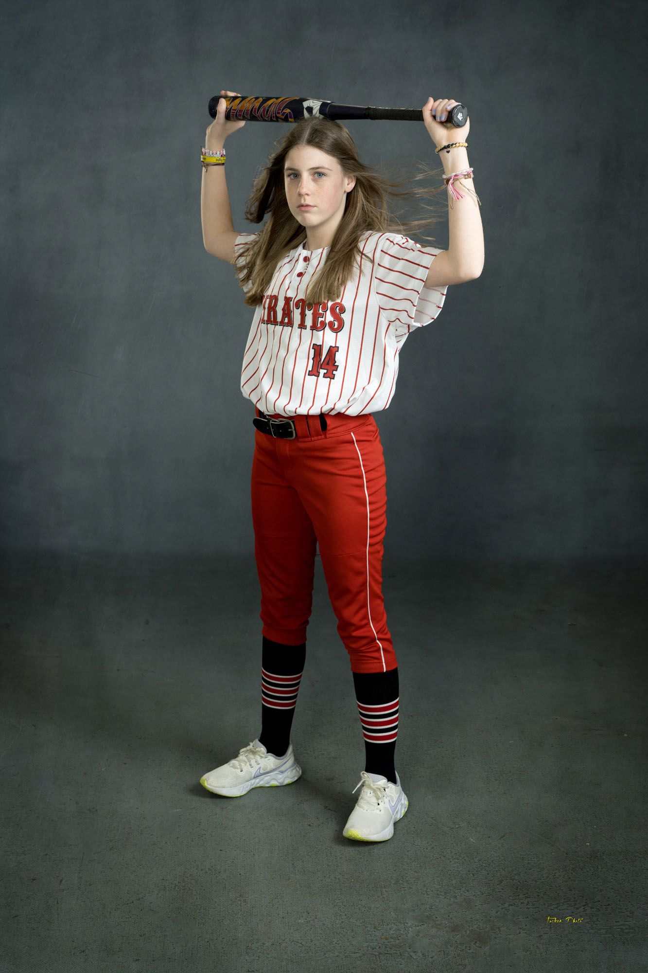 Young Pirates softball player number 14 holding bat overhead in dynamic studio pose.