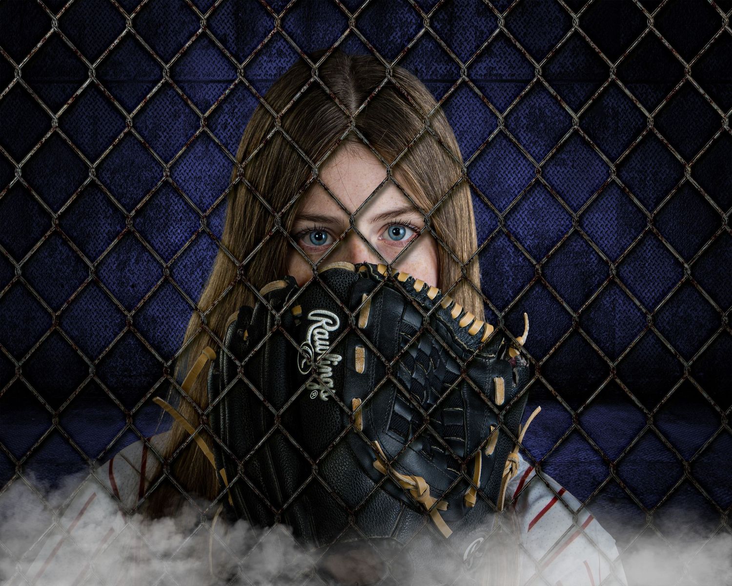 Young girl holding a Rawlings baseball glove over her face behind a chain-link fence.