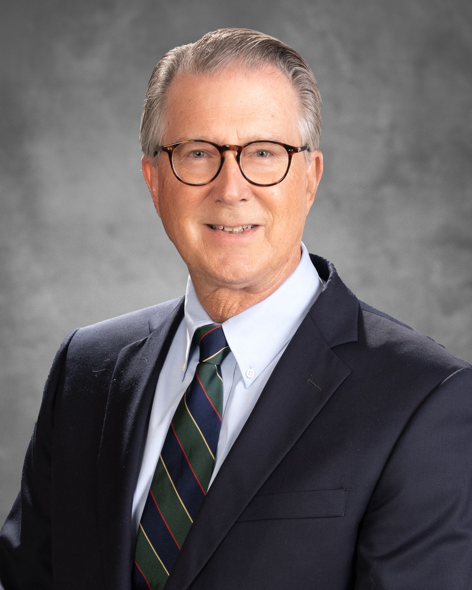 Professional senior man in navy suit and striped tie poses for formal business headshot portrait.