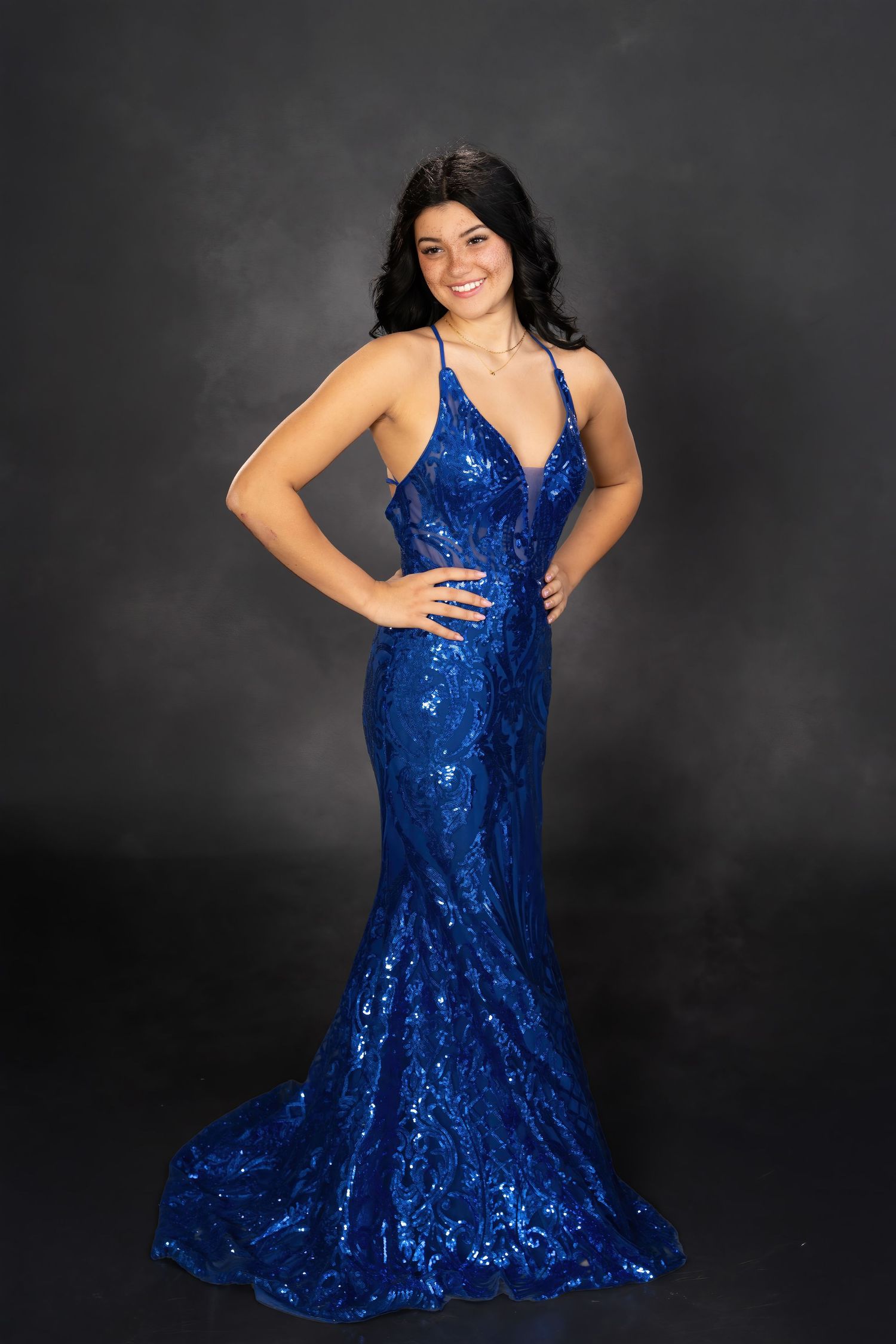 Woman in royal blue sequin mermaid gown posing against dark gray background.
