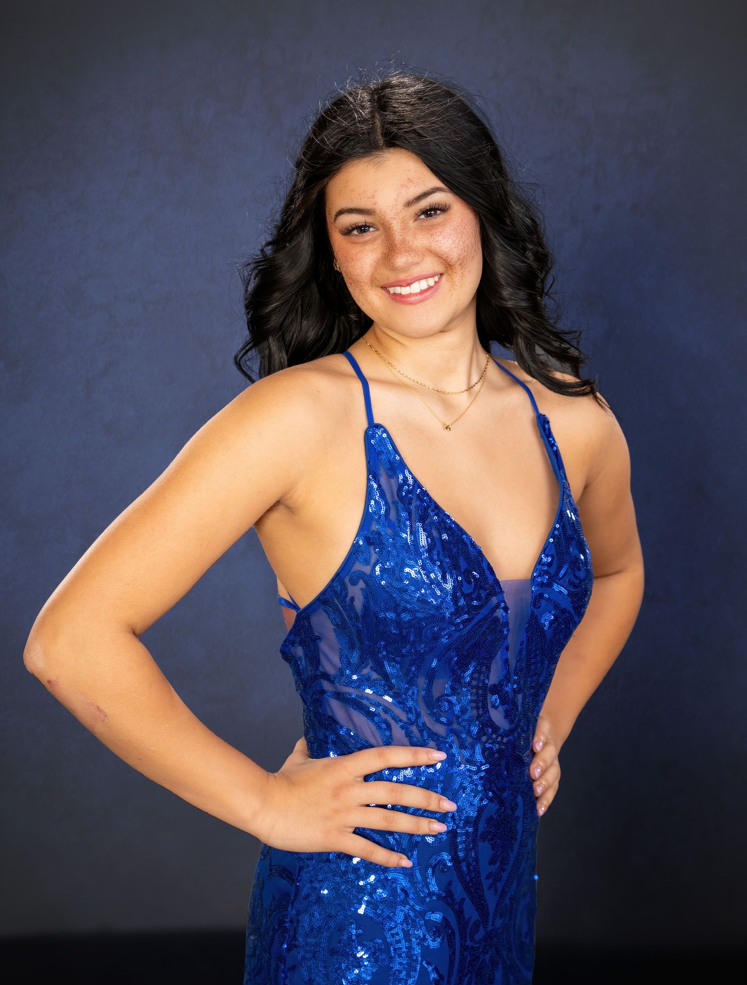 Young woman smiling in a blue sequin formal gown posing for prom photos.