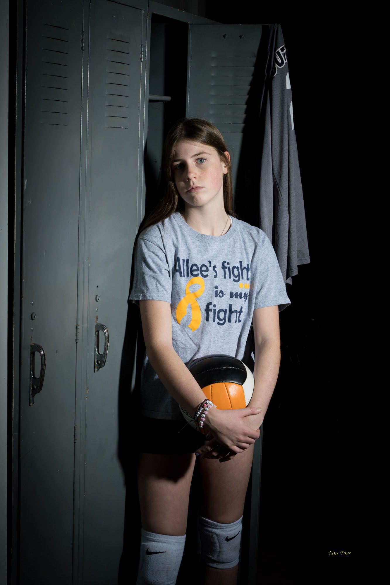 Young volleyball player in locker room wearing Allee's Fight awareness shirt holding a volleyball.