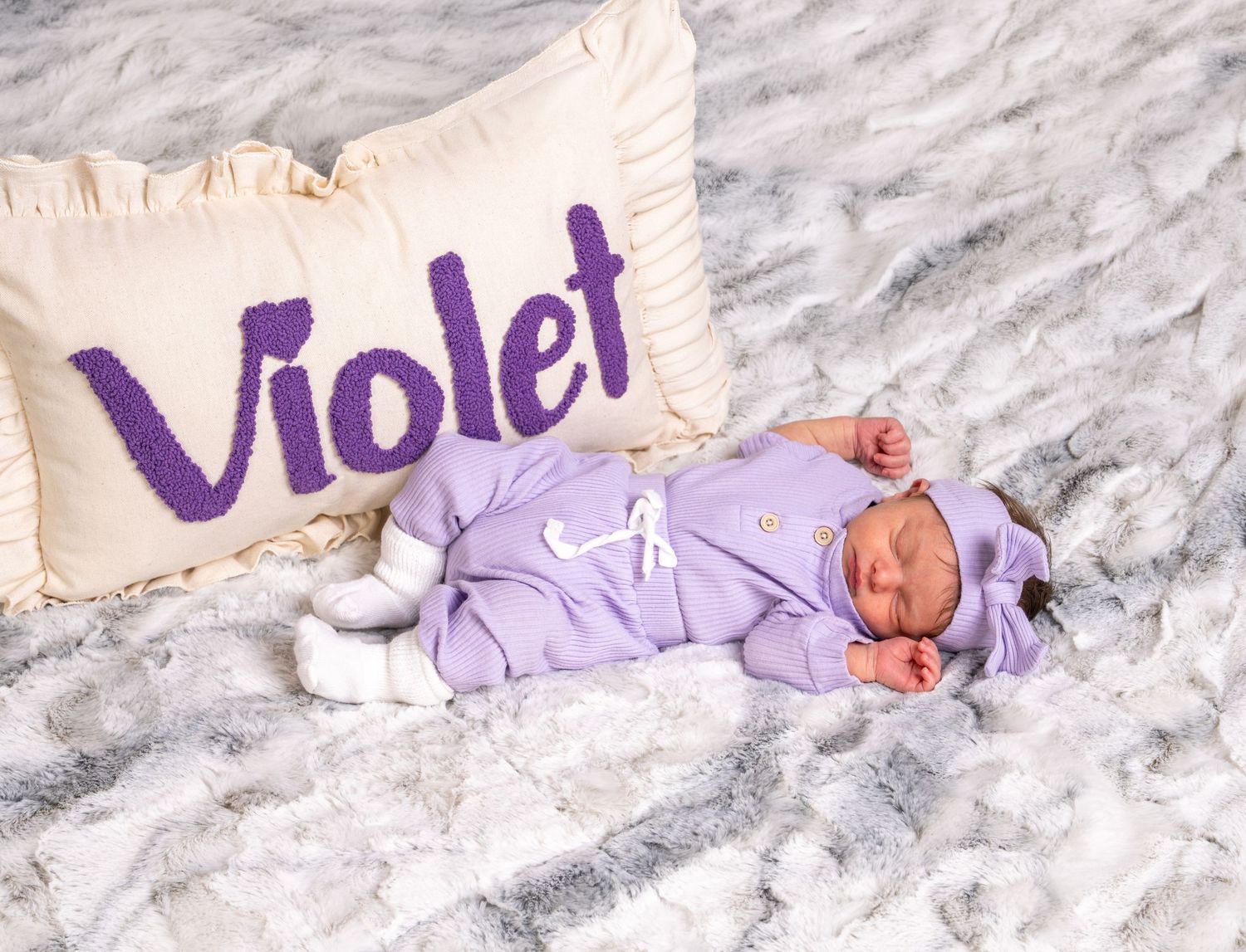 Newborn baby in purple outfit sleeping beside name pillow reading Violet.