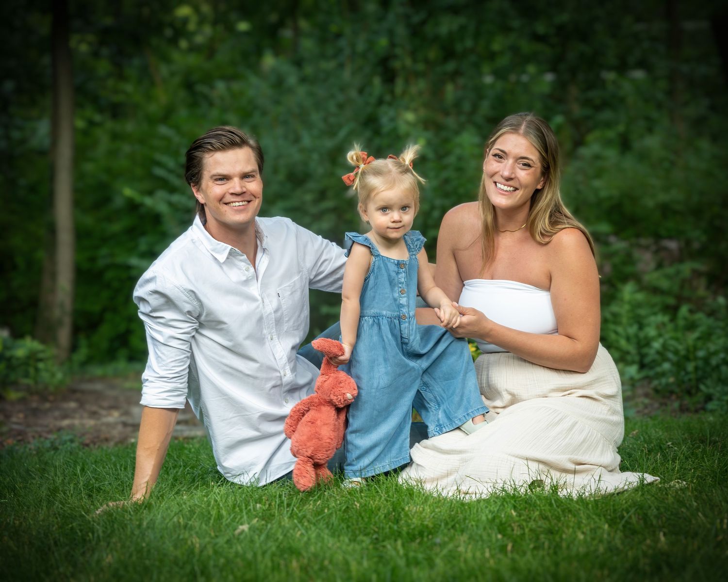 Young couple sitting on grass with toddler girl holding red toy.