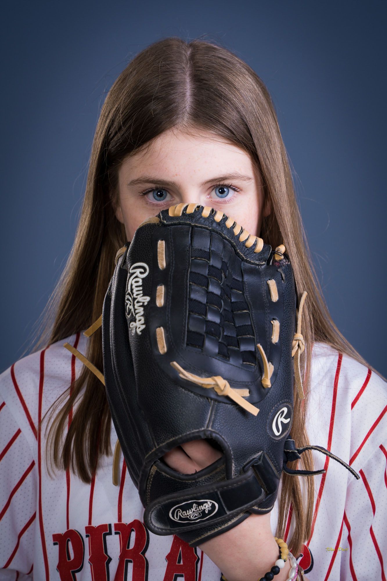 Young female softball player hiding face behind black Rawlings catcher's glove.