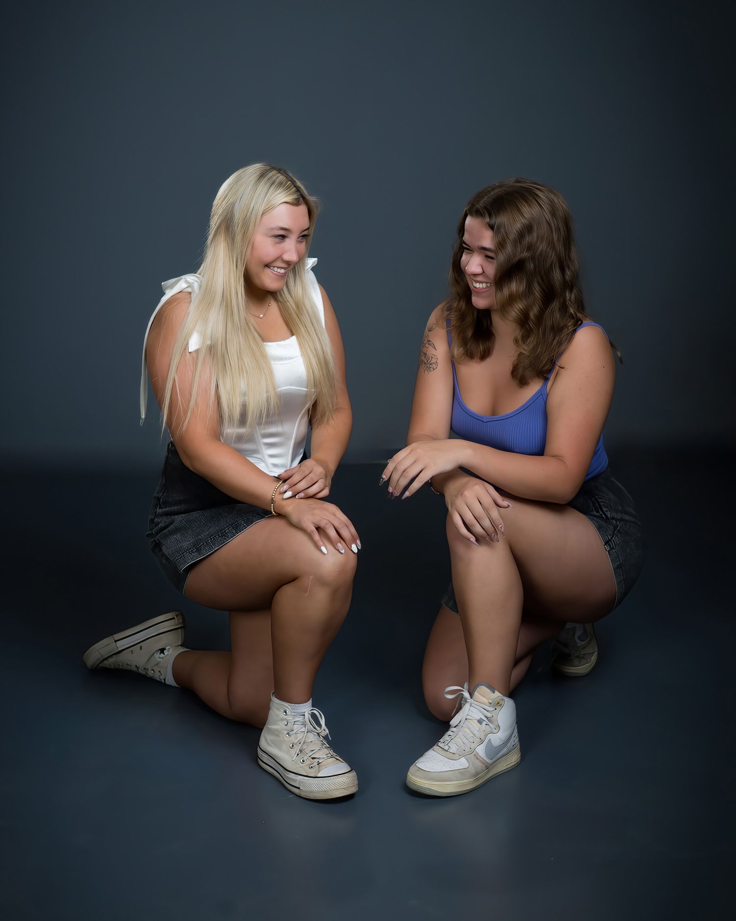 Two teenage girls, blonde and brunette, smiling at each other during a studio portrait session.