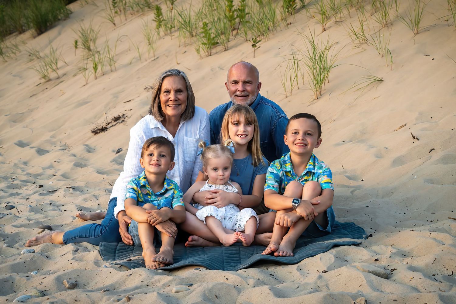 Grandparents with four grandchildren posing on sandy beach dunes together.