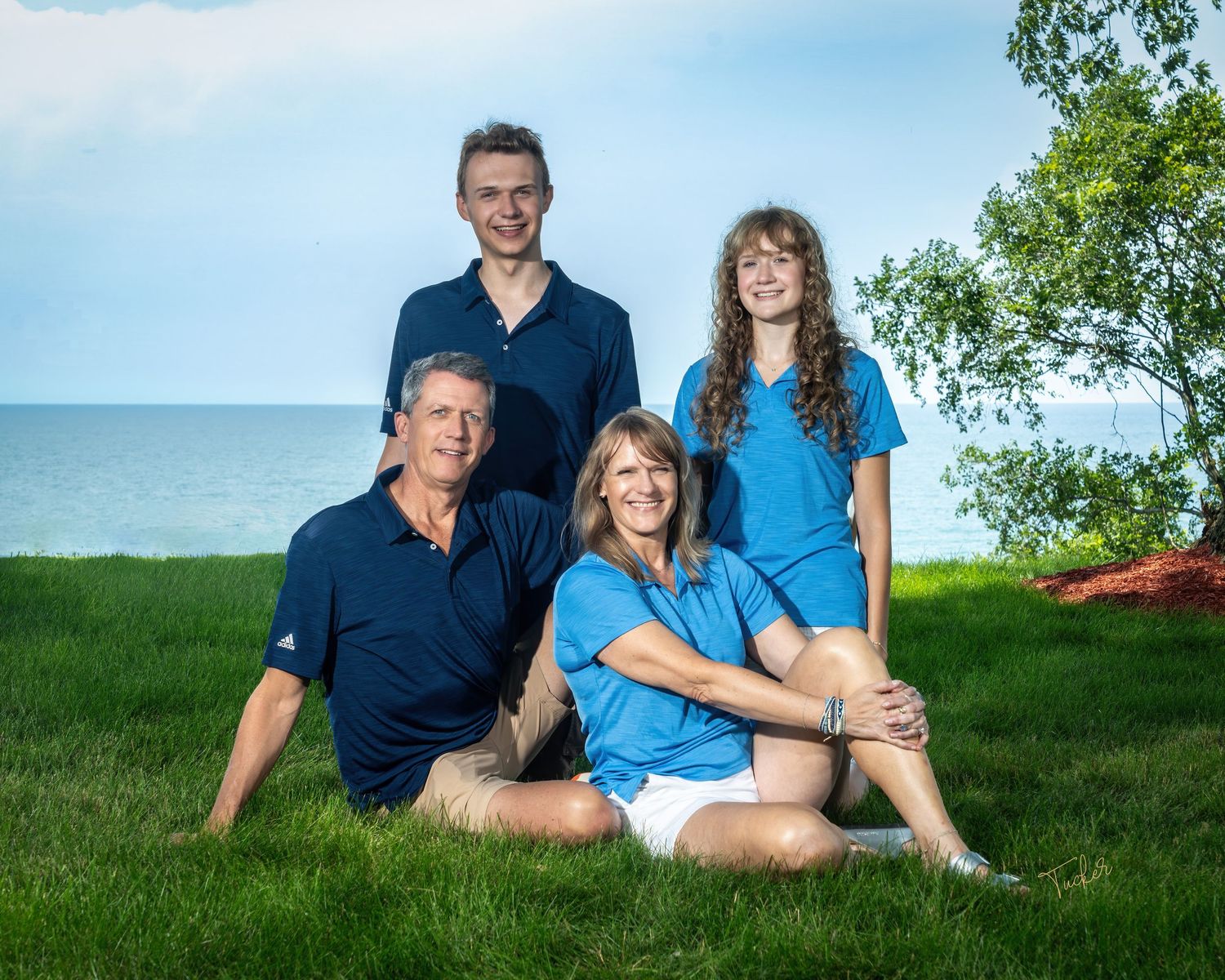 Family of four posing on grass near lakeside, two adults seated and two teens standing behind them.