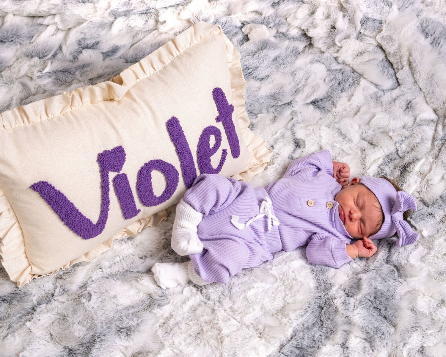 Sleeping newborn baby named Violet in purple outfit beside personalized name pillow.