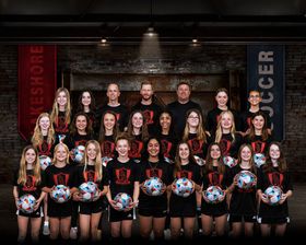 Lakeshore girls soccer team poses for group photo in red and black uniforms holding soccer balls.