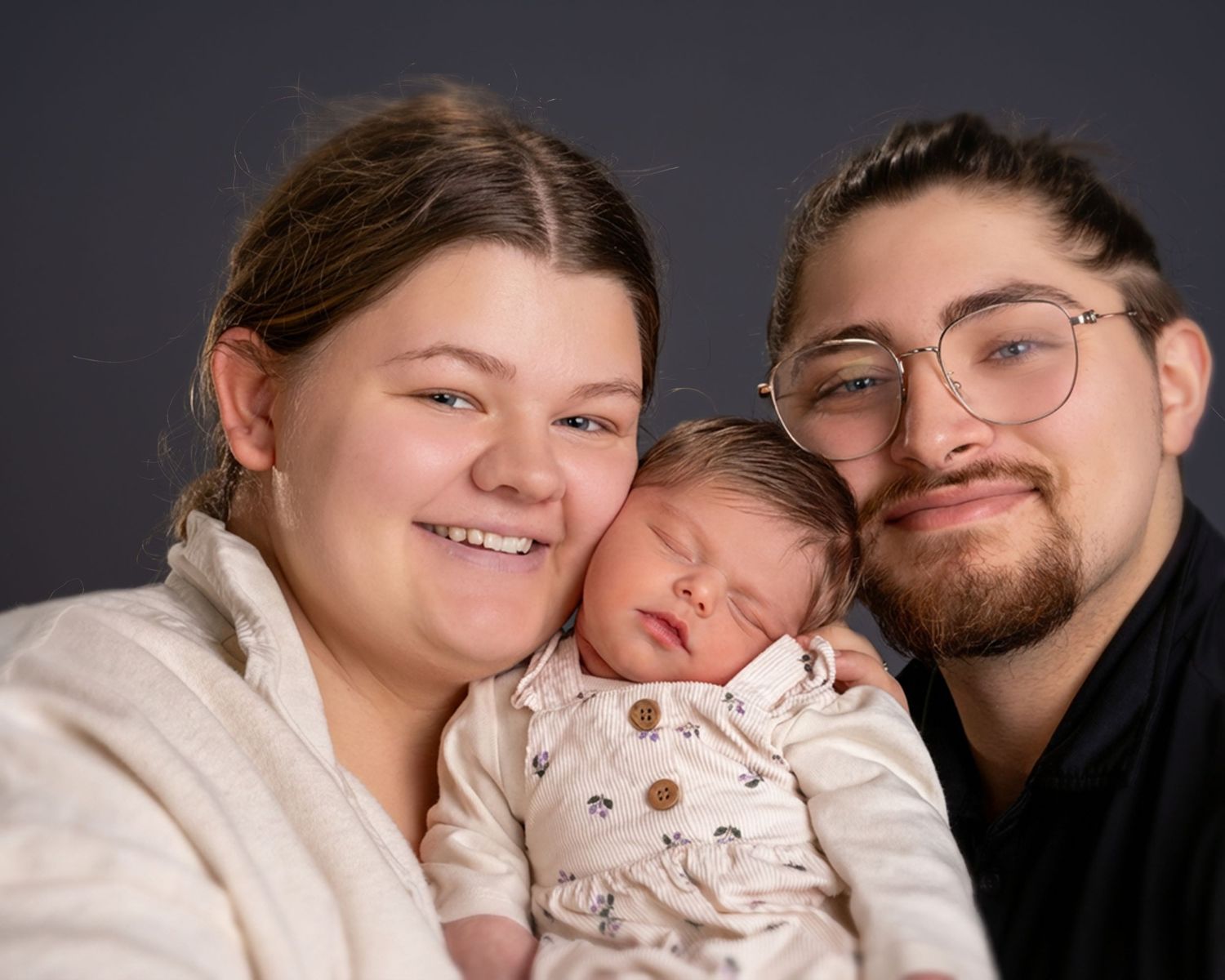 Young couple smiling with sleeping newborn baby in professional studio portrait photography.