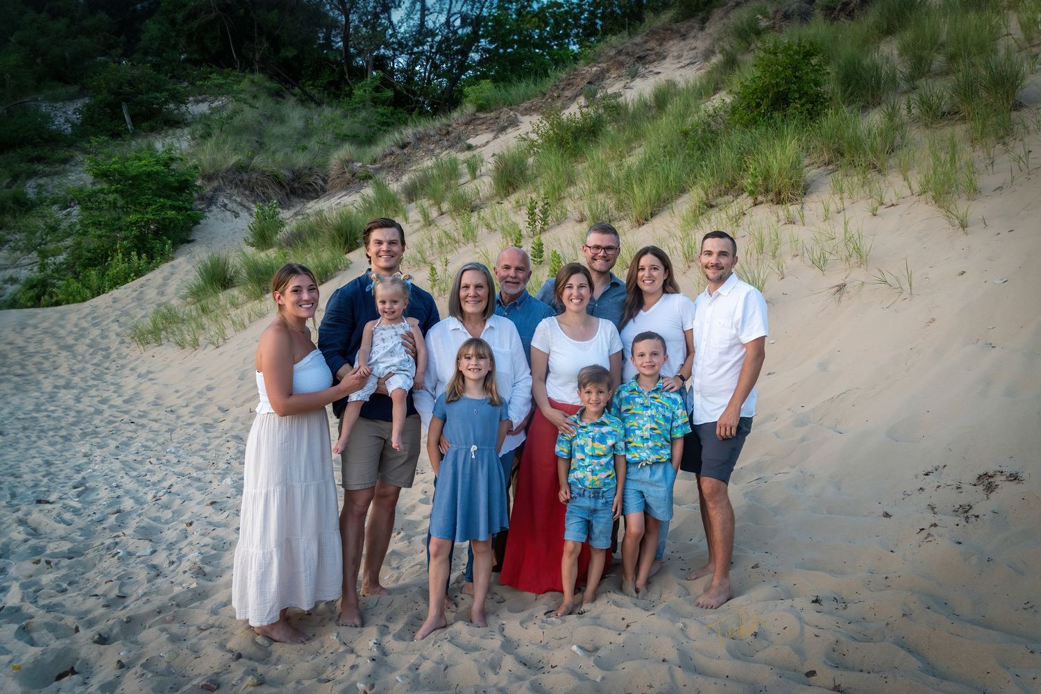 Large extended family group portrait on sandy beach with grass dunes.