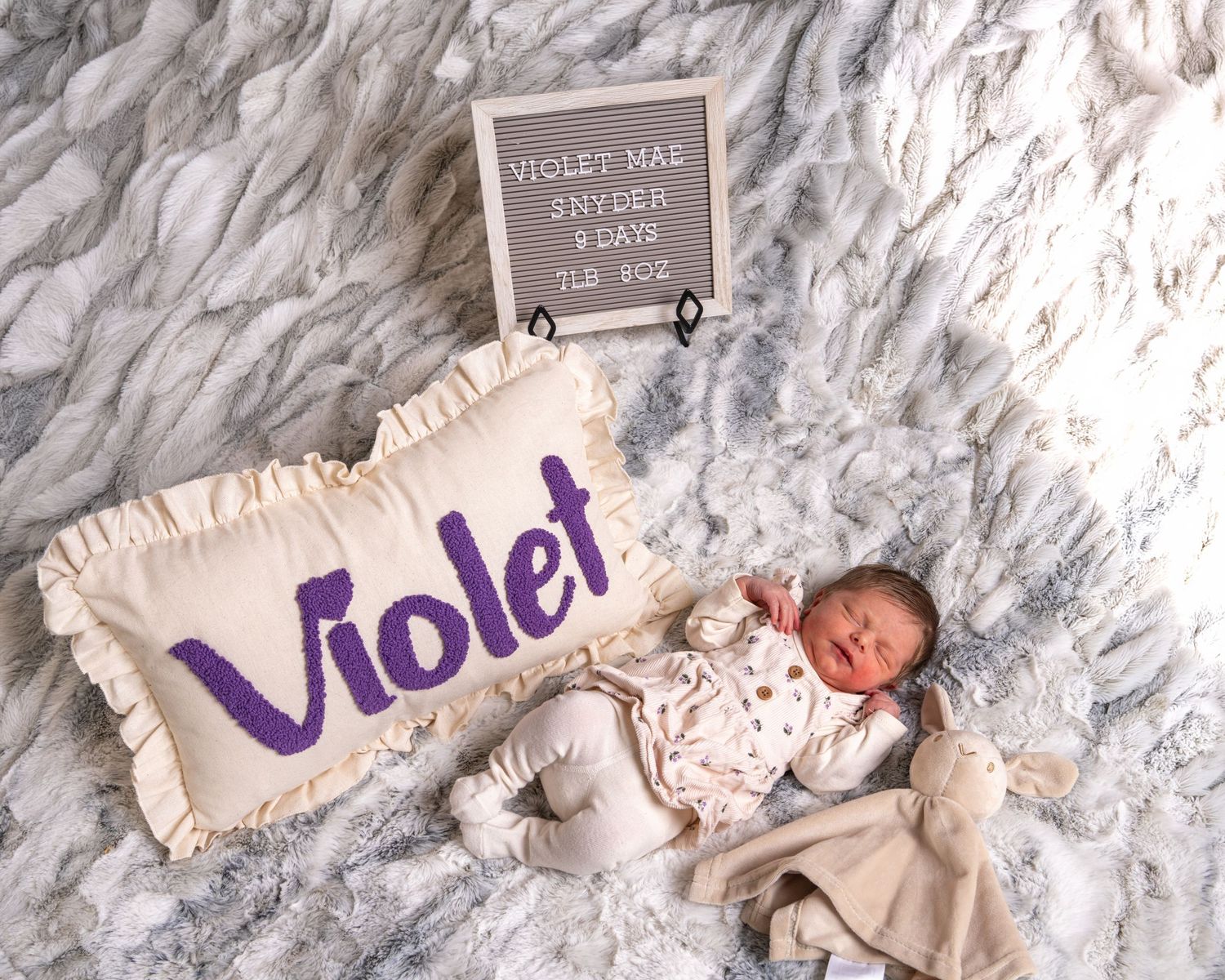 Newborn baby Violet Mae Snyder lying beside name pillow and letter board announcement.