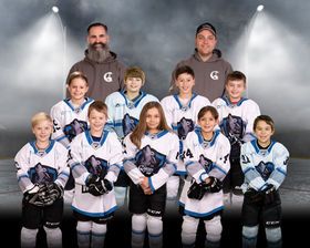 Youth hockey team in white and blue jerseys poses with coaches for official team photo.