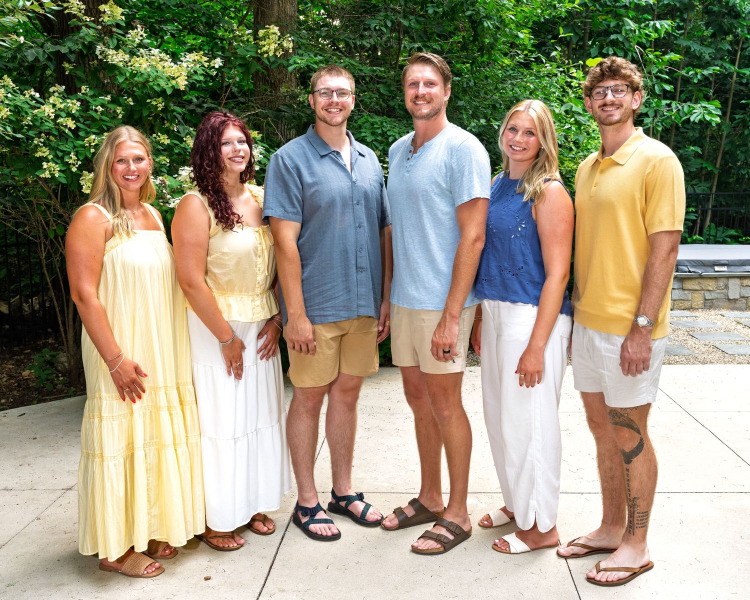 Group of six adults posing together outdoors in coordinated yellow and white outfits.