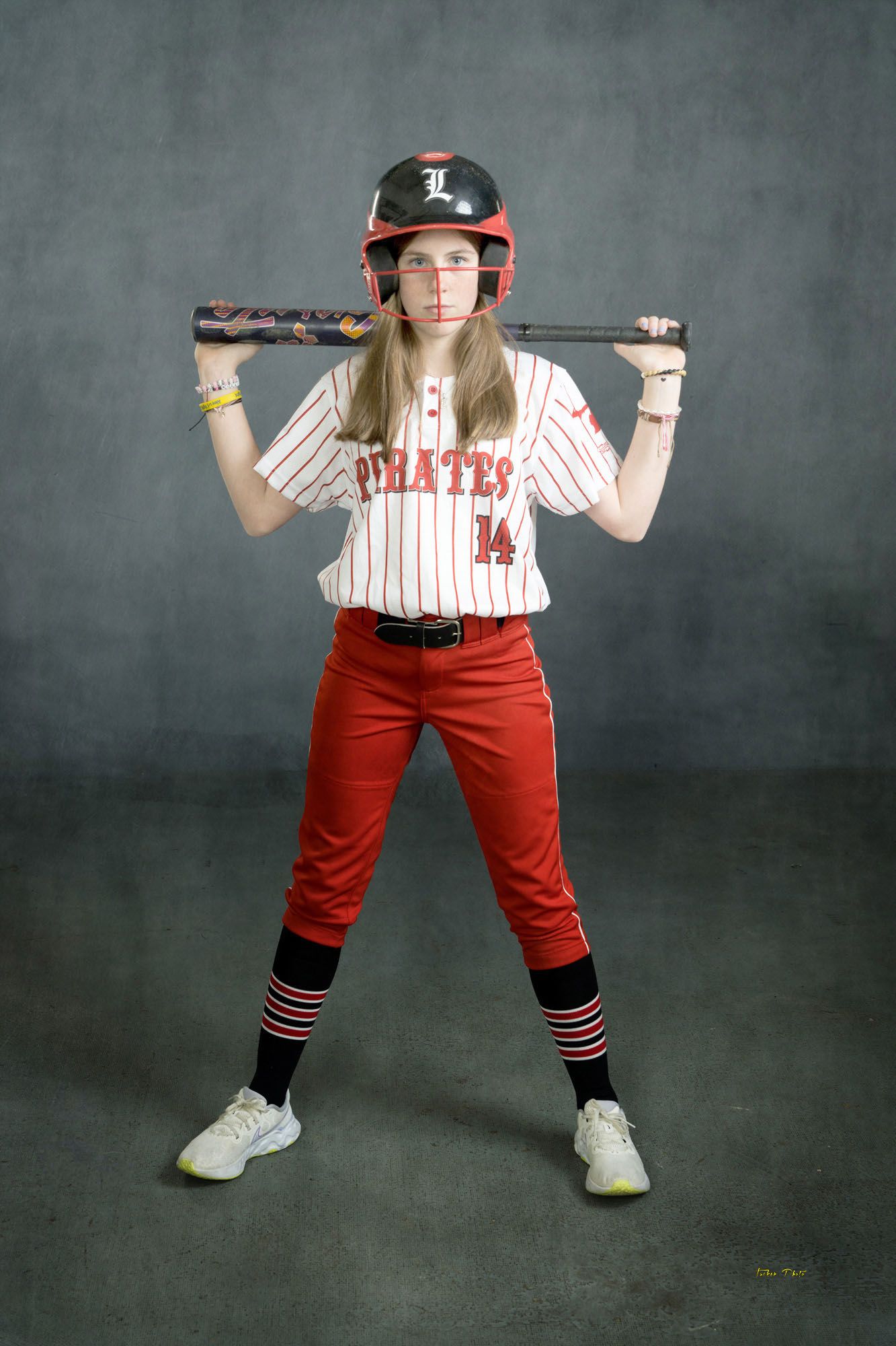 Female Pirates softball player #14 poses with bat on shoulders wearing red and white pinstripe uniform and red helmet.