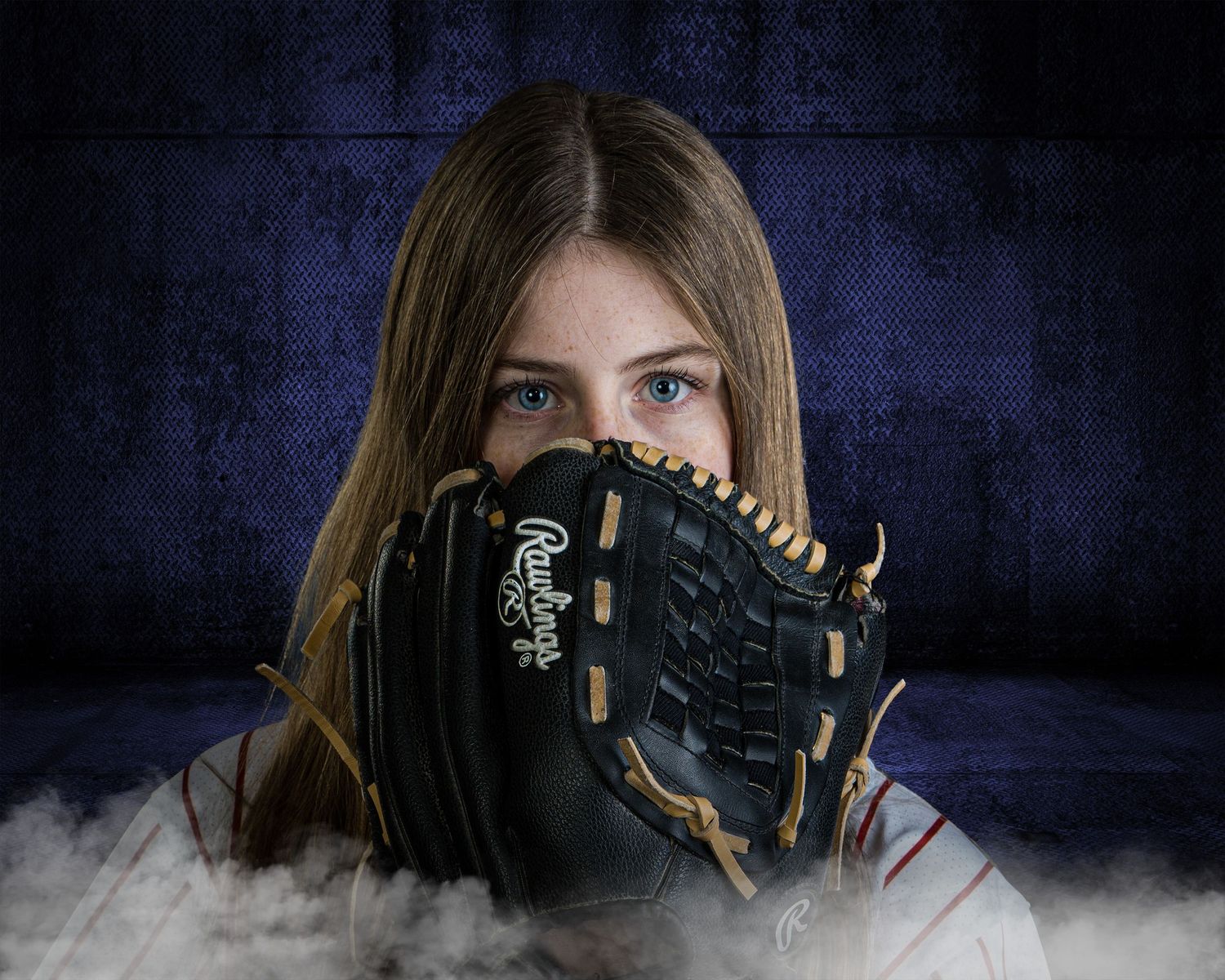 Girl holding a Rawlings baseball glove up to her face with blue eyes visible against a dark blue background.
