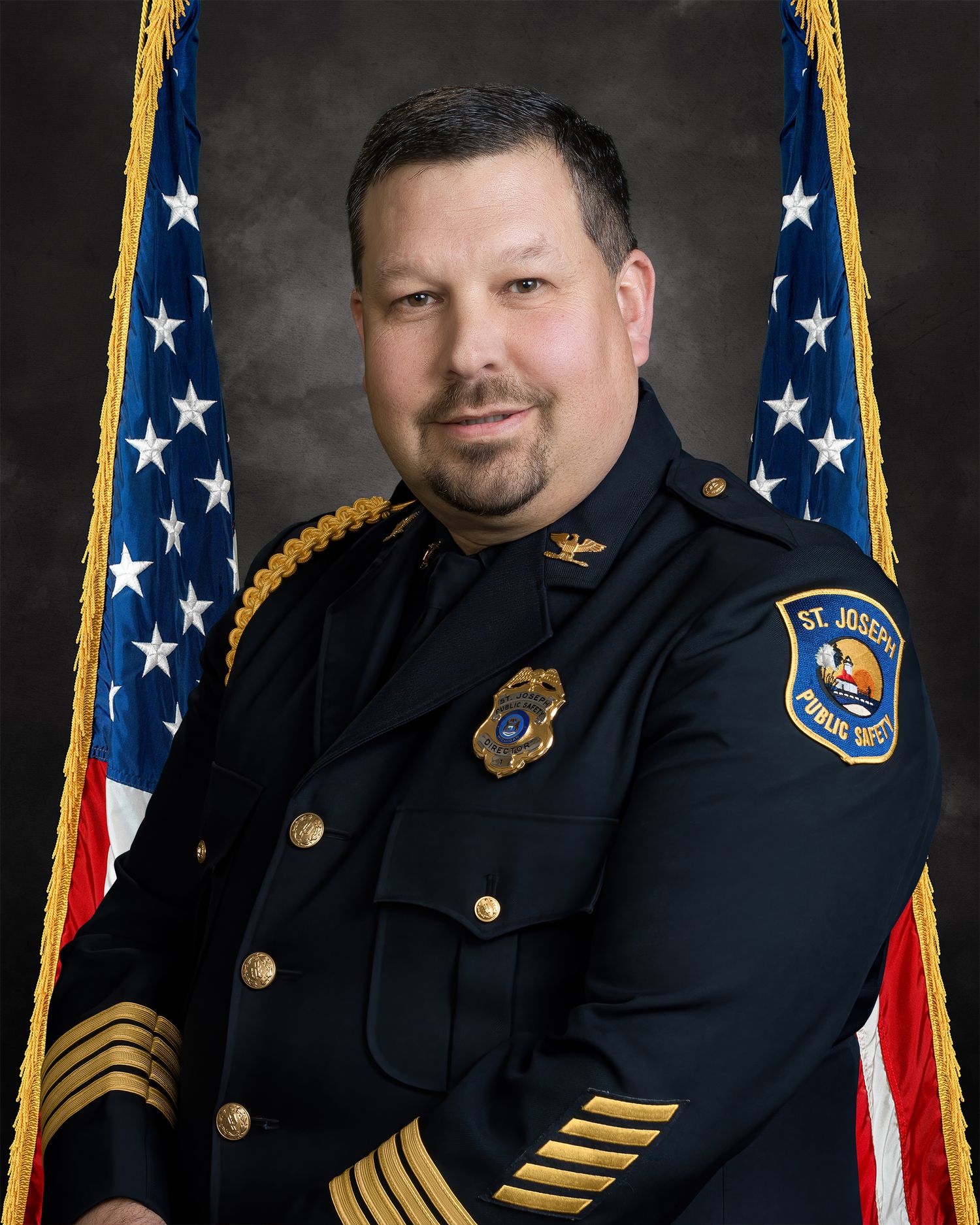 St. Joseph Public Safety police chief in dress uniform posing before American flags in an official portrait.