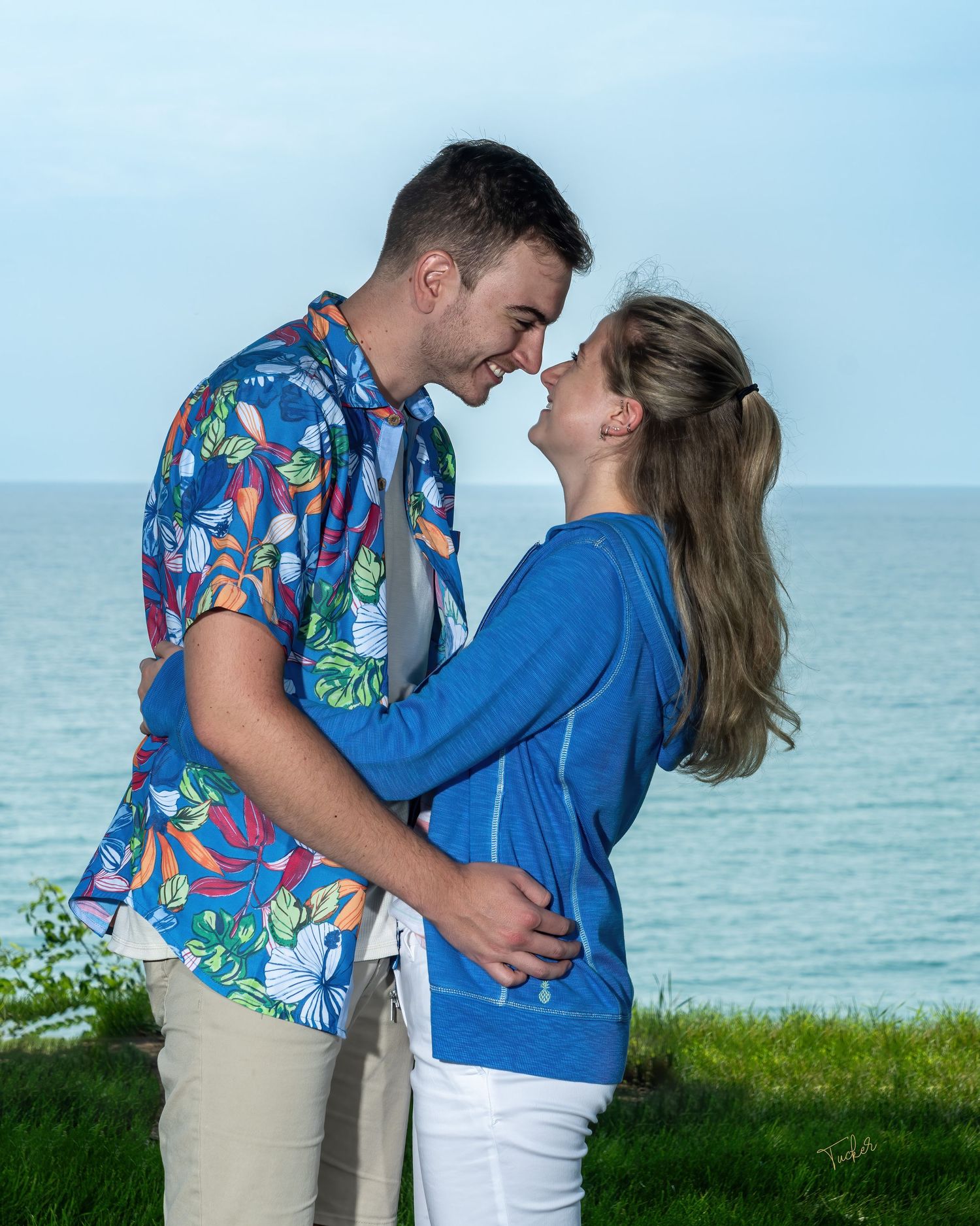 Young romantic couple embracing and leaning in for a kiss outdoors near the ocean shoreline.