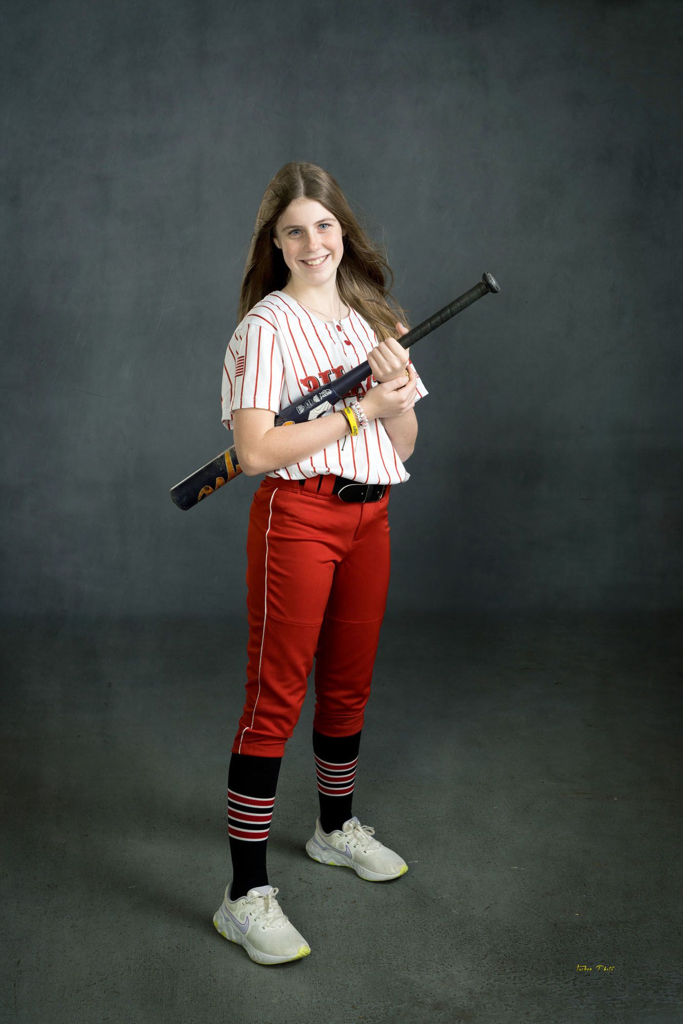 Smiling young softball player in Pirates pinstripe uniform holding black bat over shoulder.