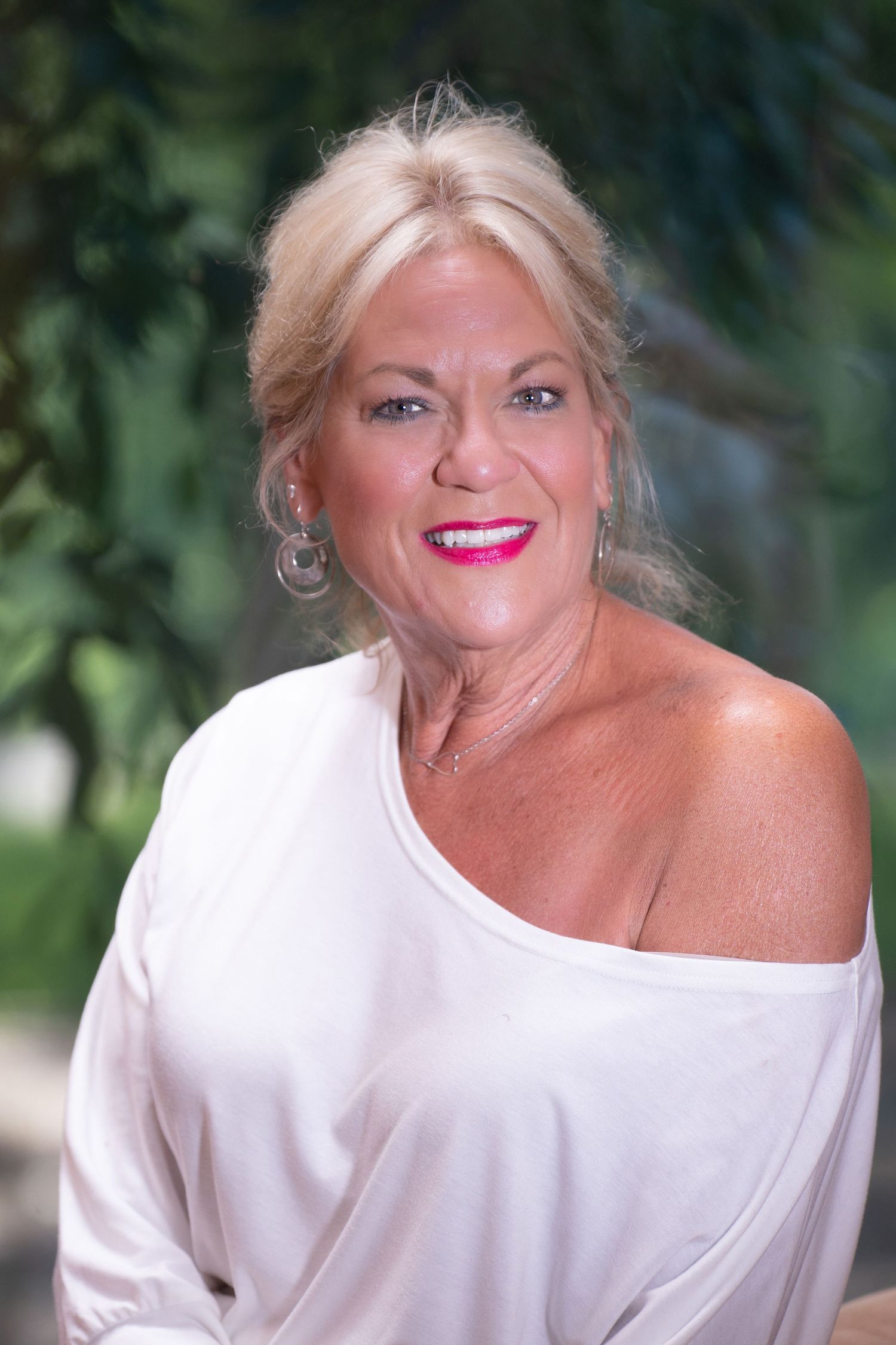 Close-up portrait of smiling blonde woman in white off-shoulder top with pink lips outdoors.