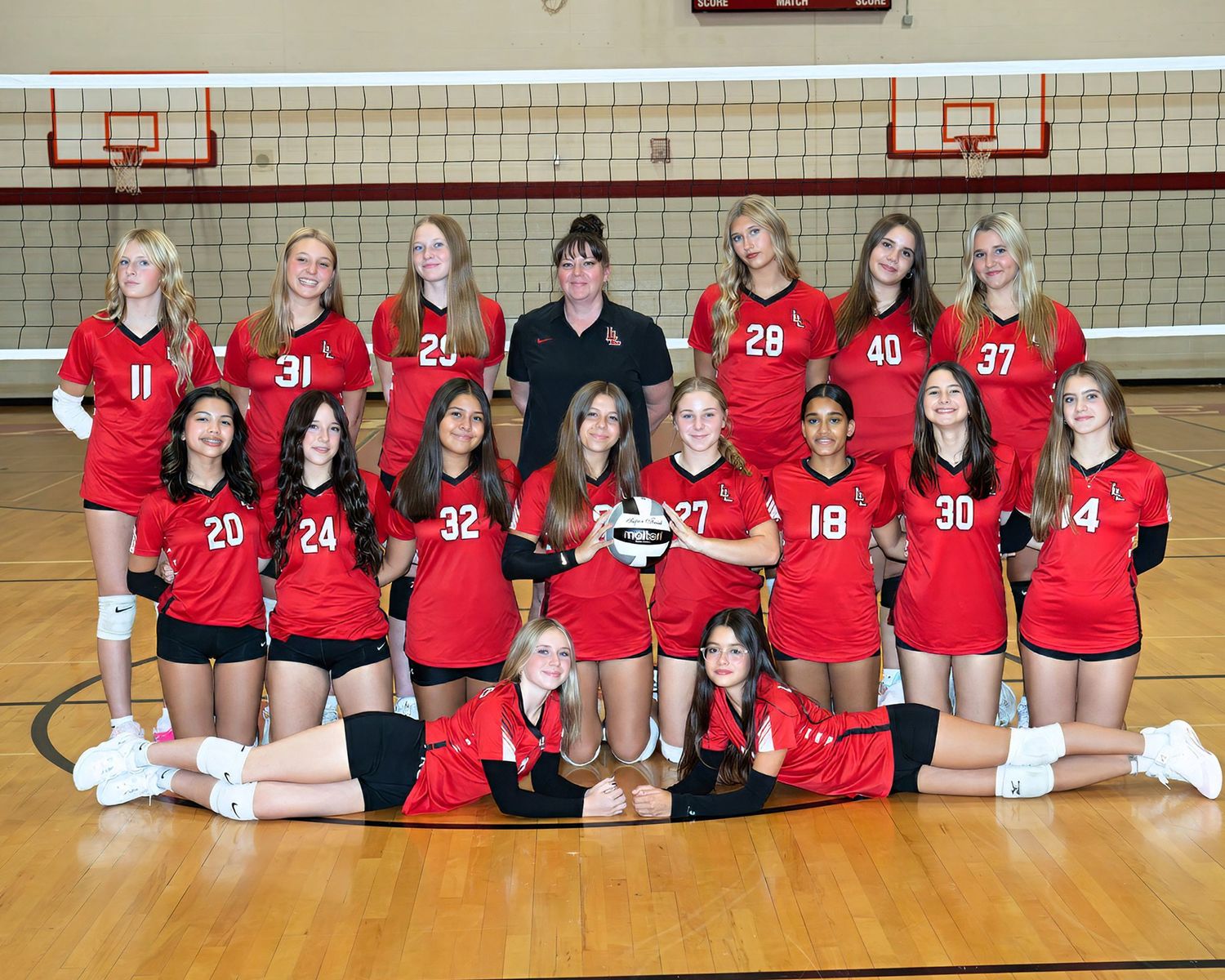Middle school girls volleyball team in red uniforms posing with trophy in gymnasium.