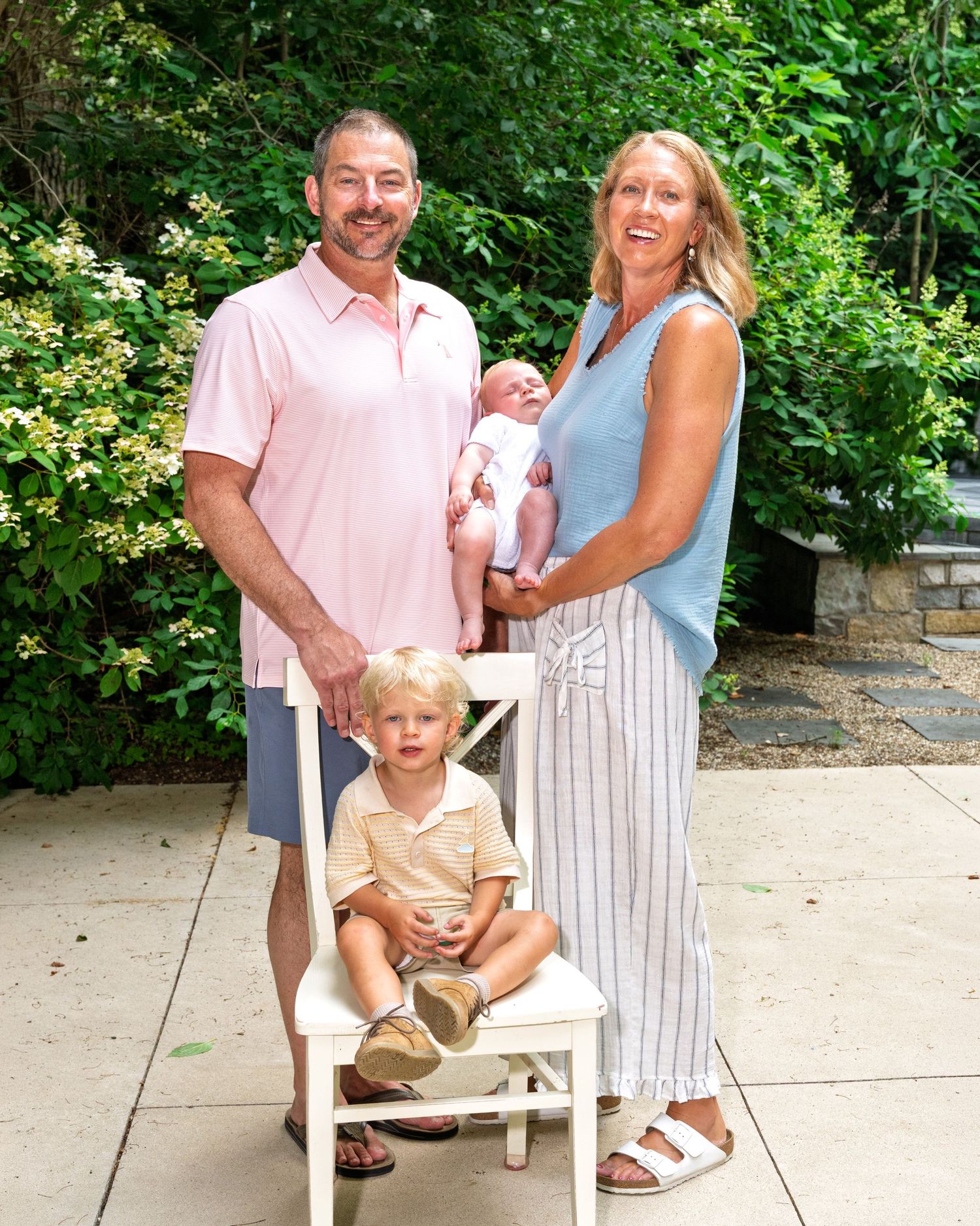 Couple with newborn baby and young toddler posing for family portrait in garden patio.