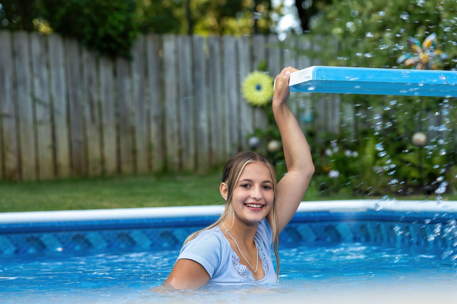 Smiling blonde teen girl plays in backyard swimming pool on a sunny summer day.