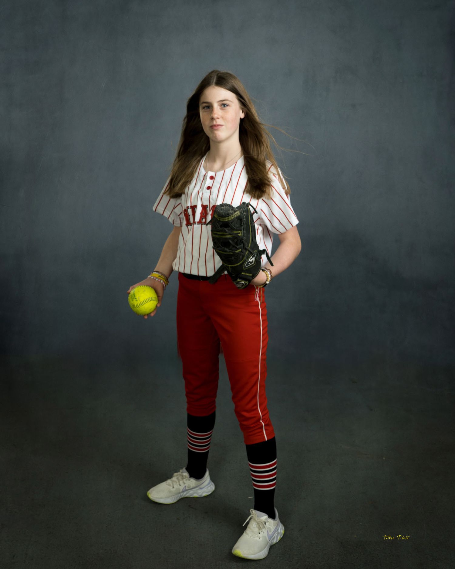 Female softball player in red and white Pirates uniform holding yellow softball and glove.