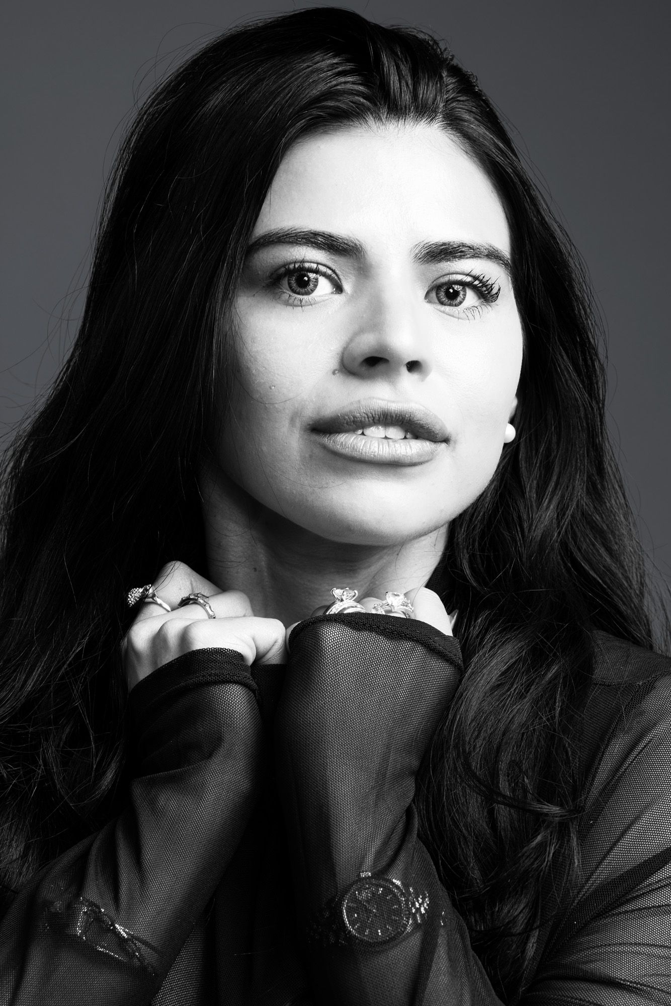 Black and white portrait of a young woman with long dark hair posing with hands raised.