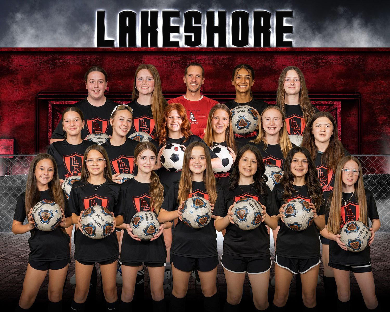Lakeshore girls soccer team poses together holding balls in front of red and black backdrop.