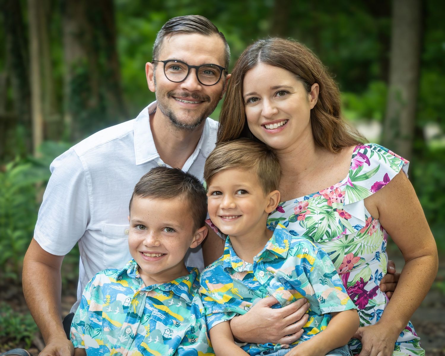 Family of four with two boys in matching shirts smiling outdoors.