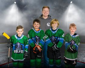 Youth hockey coach poses with four young players in green Wolves jerseys on rink backdrop.