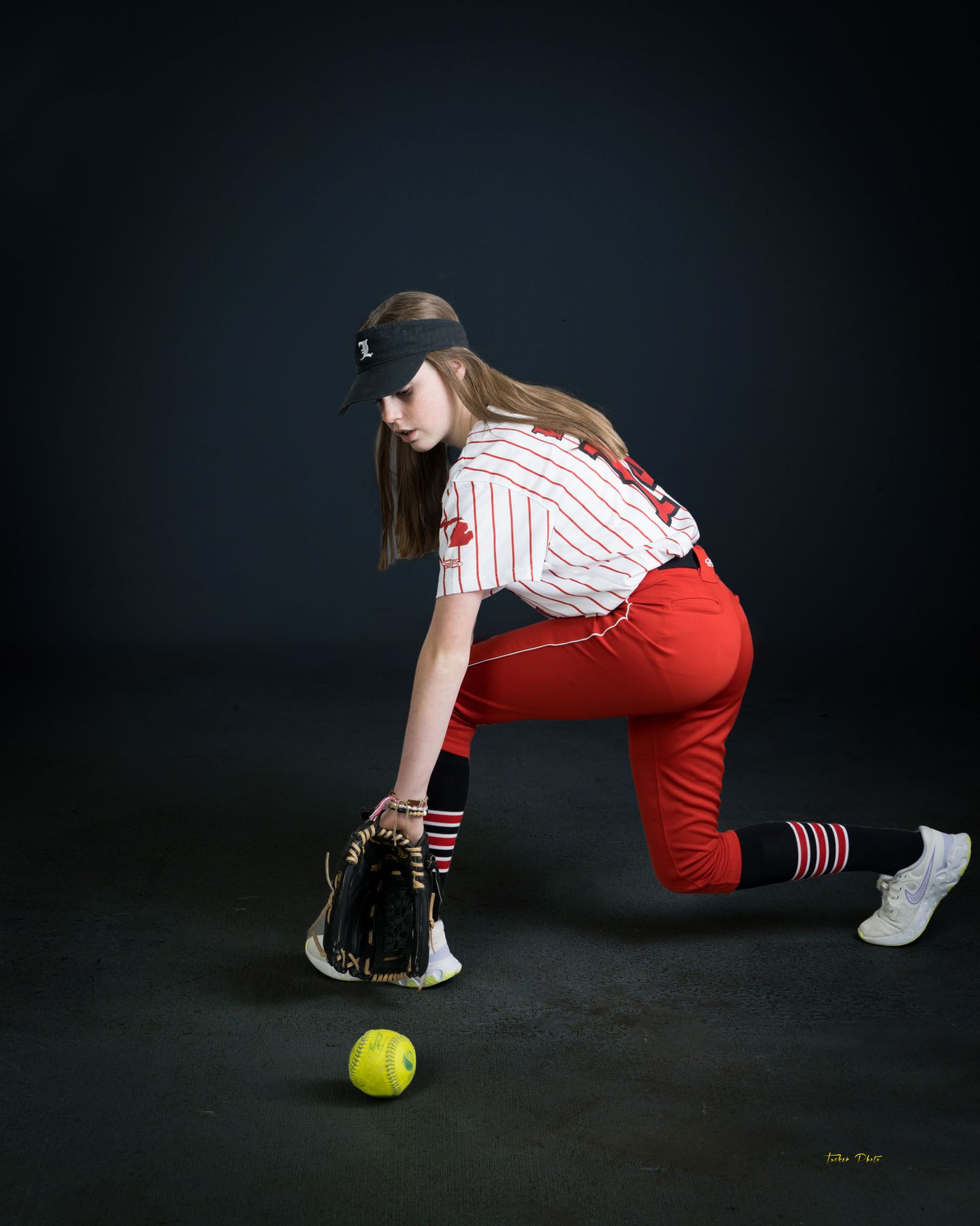 Female softball player in red uniform fielding a yellow softball with a leather glove.