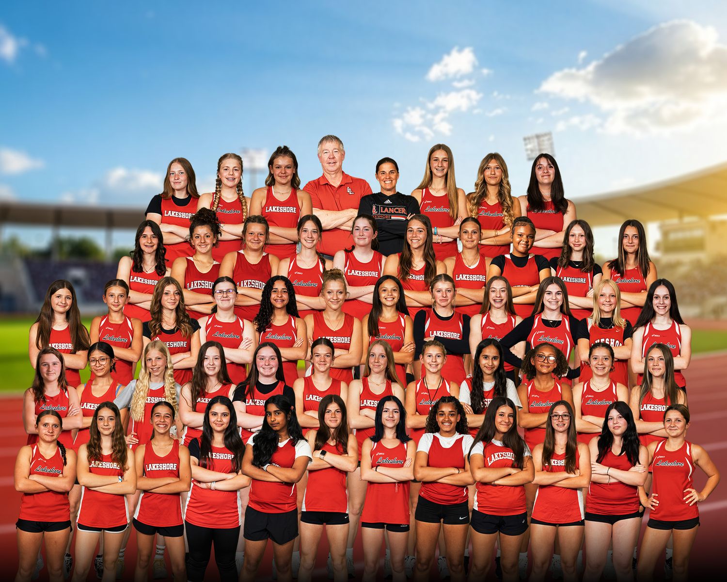 Girls track and field team photo in red uniforms posing in multiple rows outdoors.