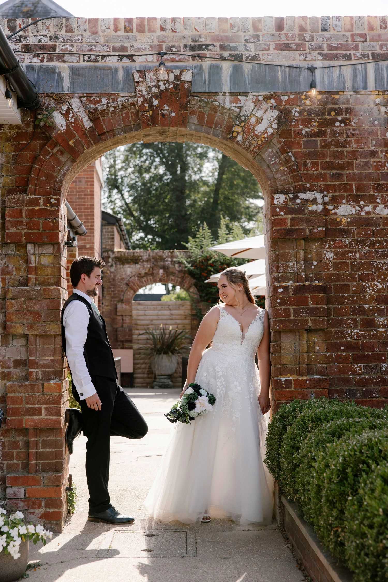 couple standing under a arch way looking at each other as the sunlight shines through
