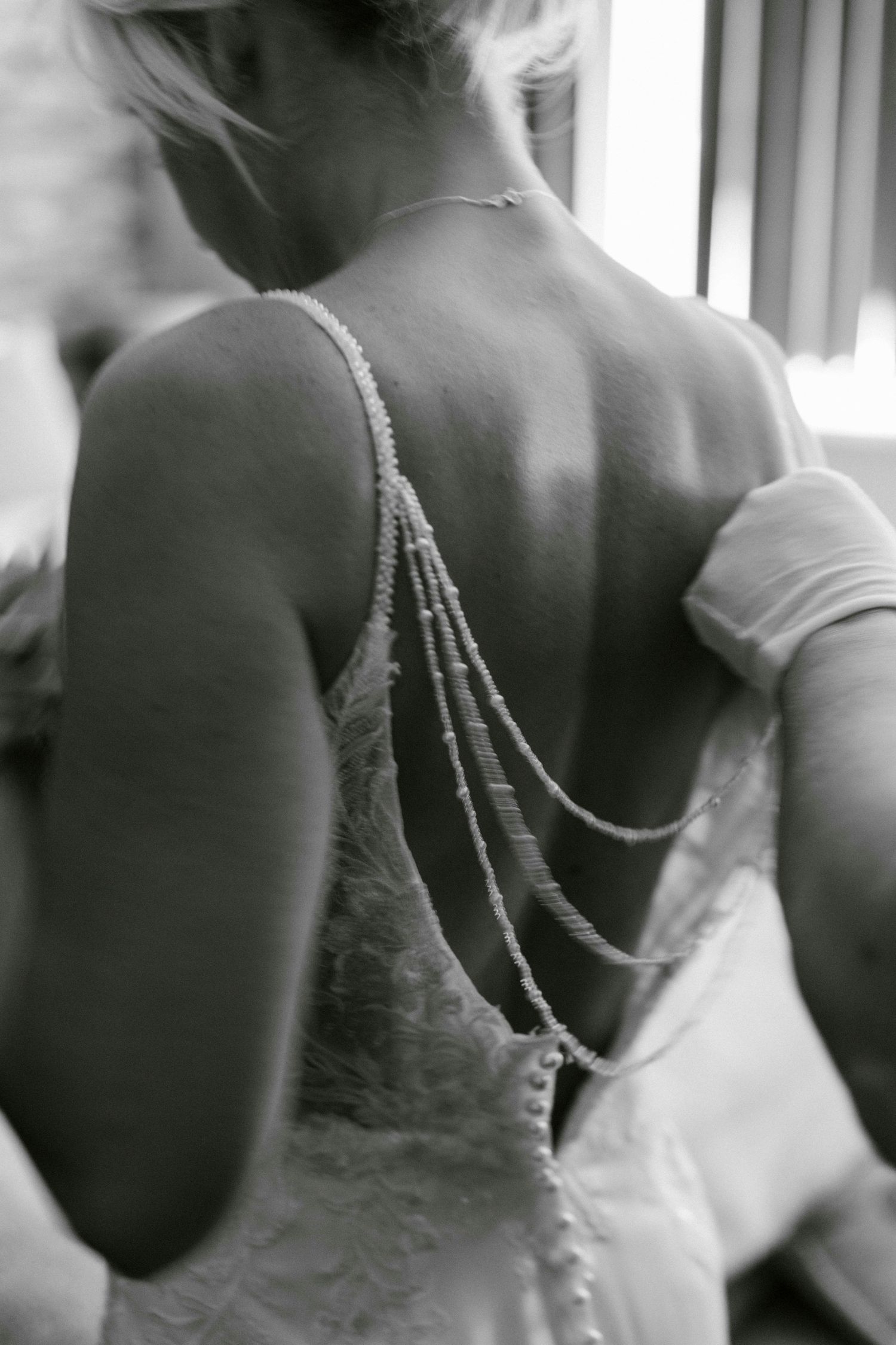 A bride having her dress done up by her mum on the morning of her wedding, in black and white.