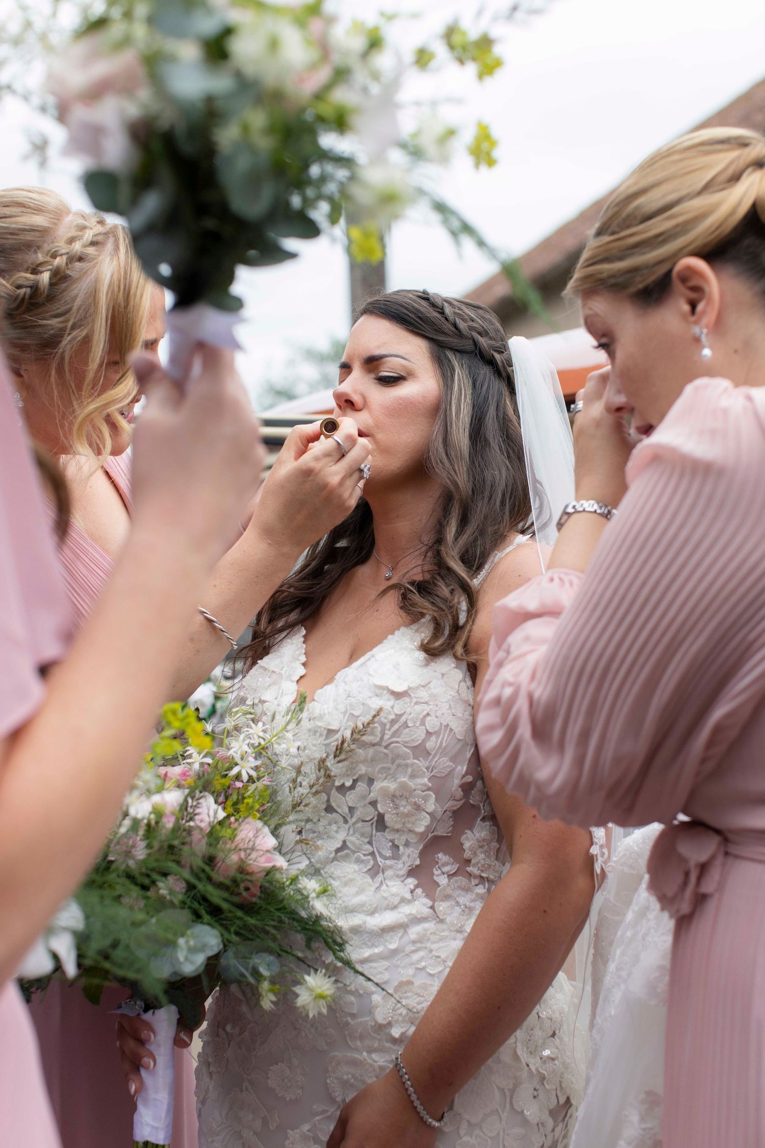 Bride in the last minutes before entering the church to marry. She is emotional and her bridesmaids are surrounding her, fixing her lipstick