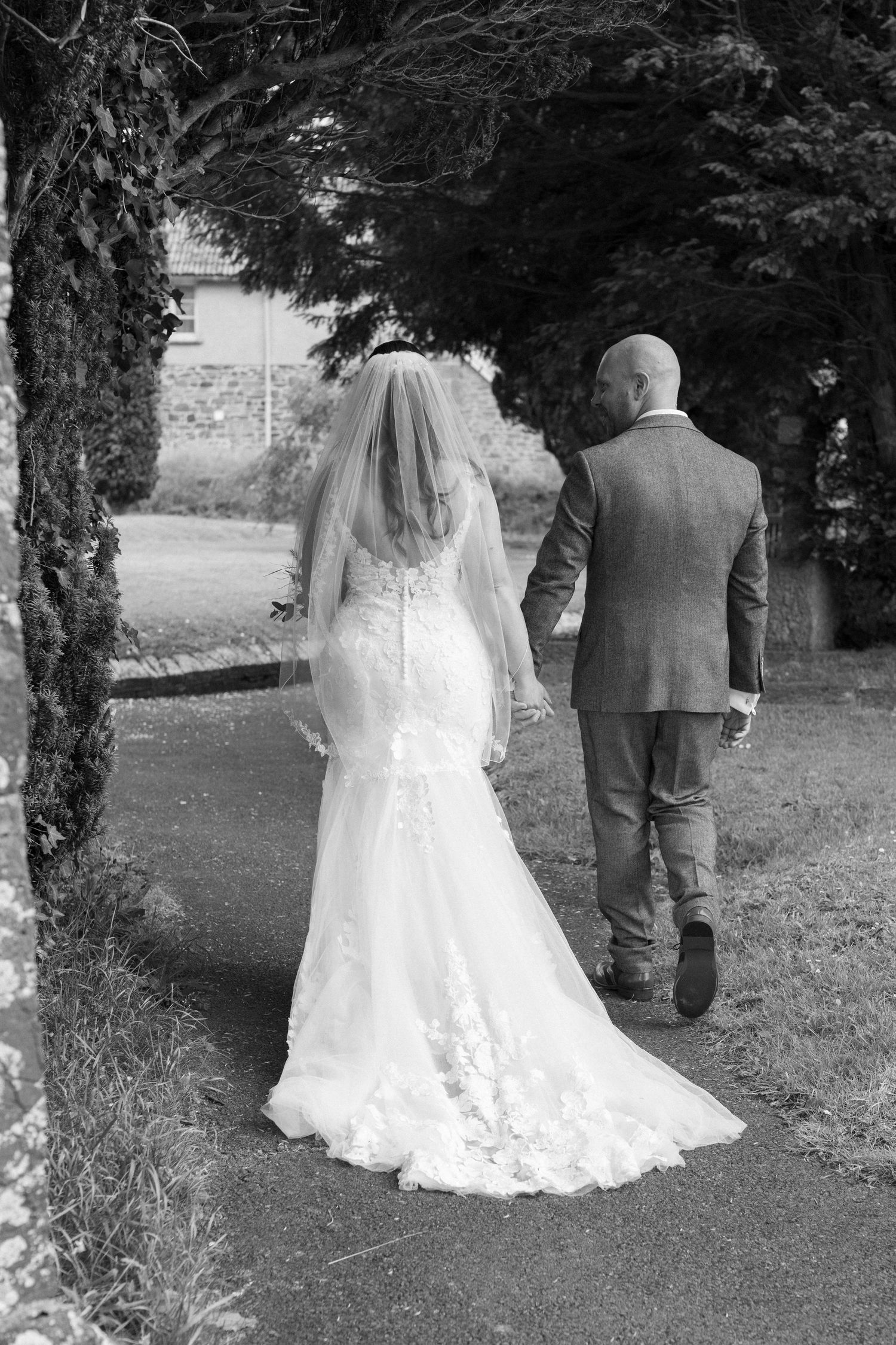 In black and white the bride and groom walking away from the camera. They are about to get their car back to the venue.